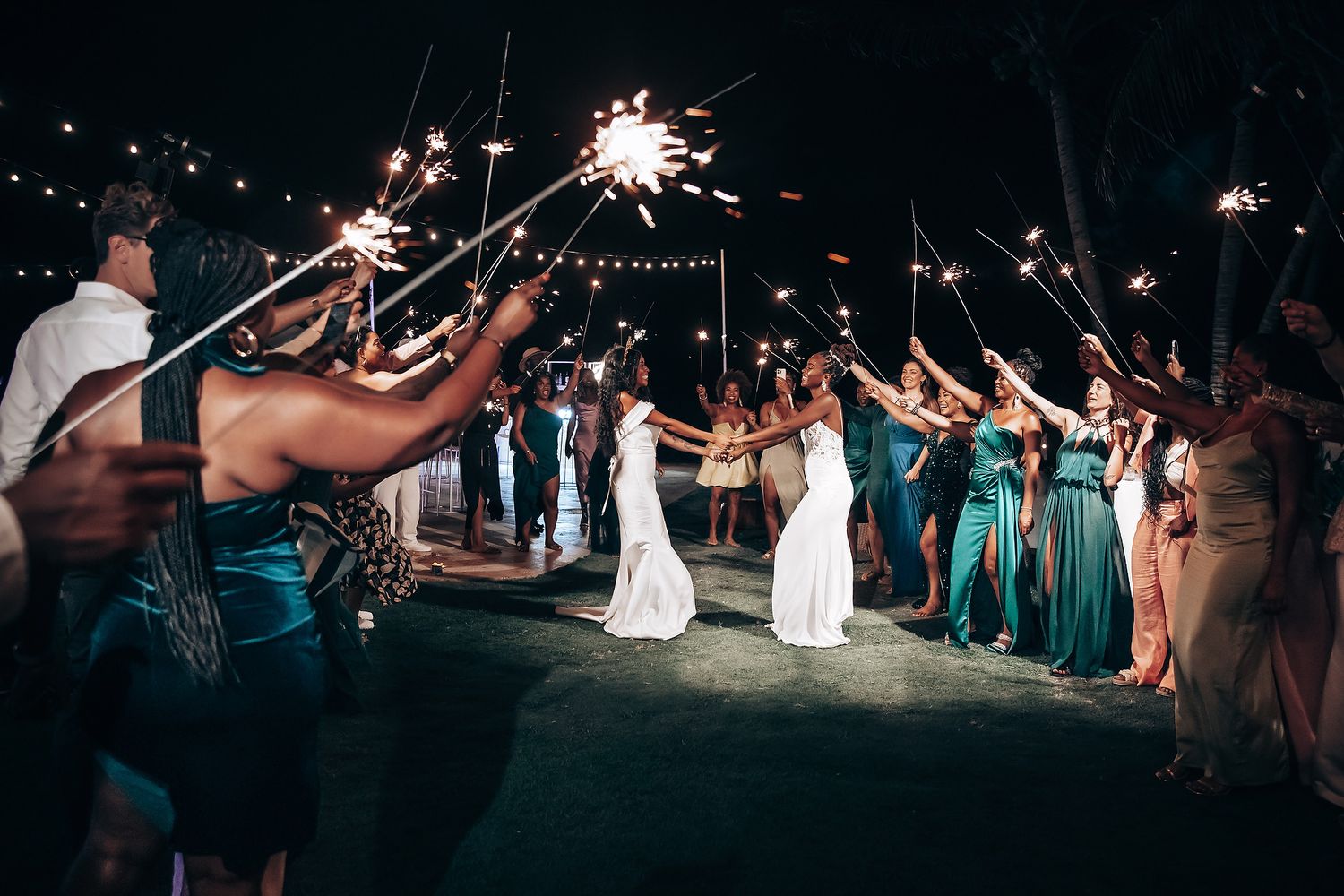 Wedding guests holding sparklers creating a magical nighttime tunnel effect.