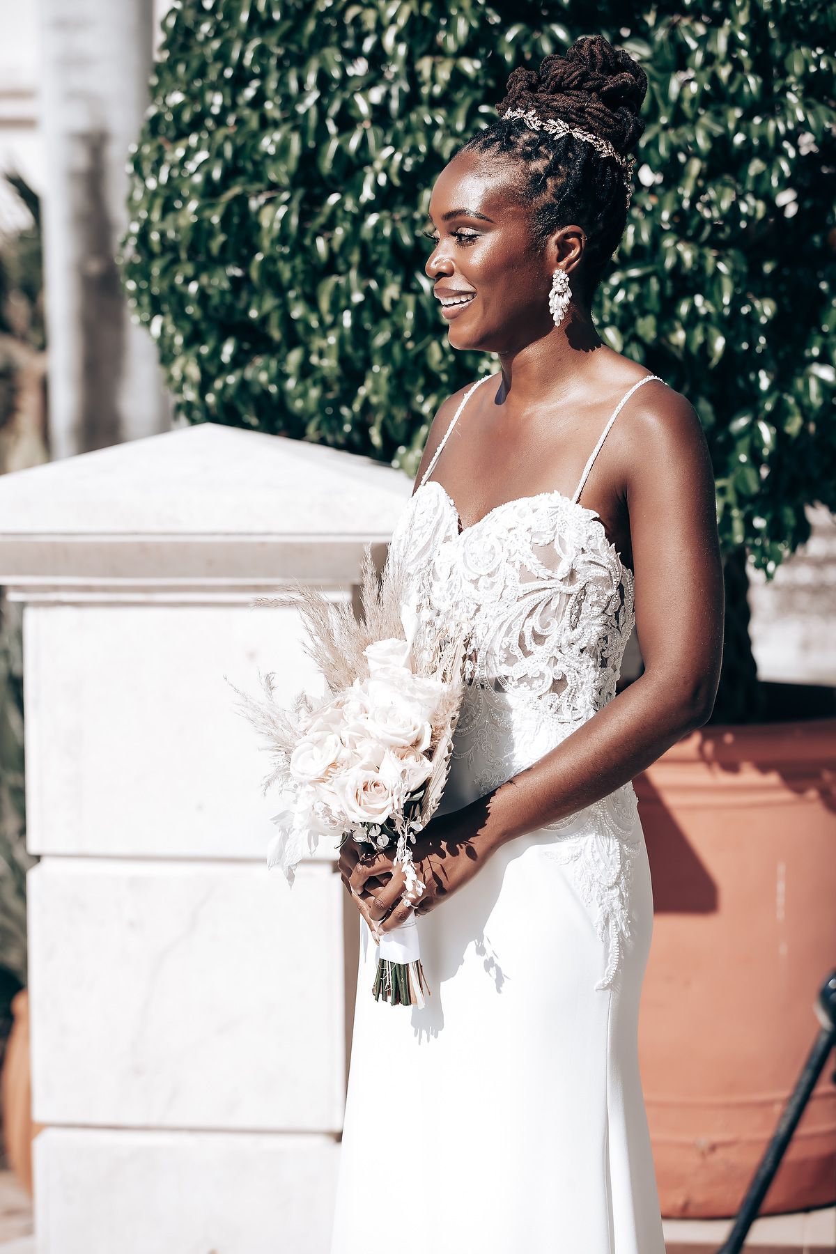Elegant white lace wedding dress captured against a leafy green background.