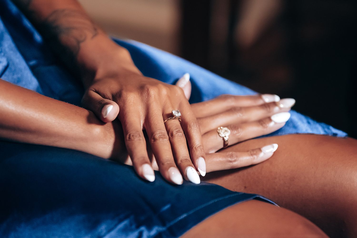 Close-up of hands with wedding rings and manicured nails against blue fabric.