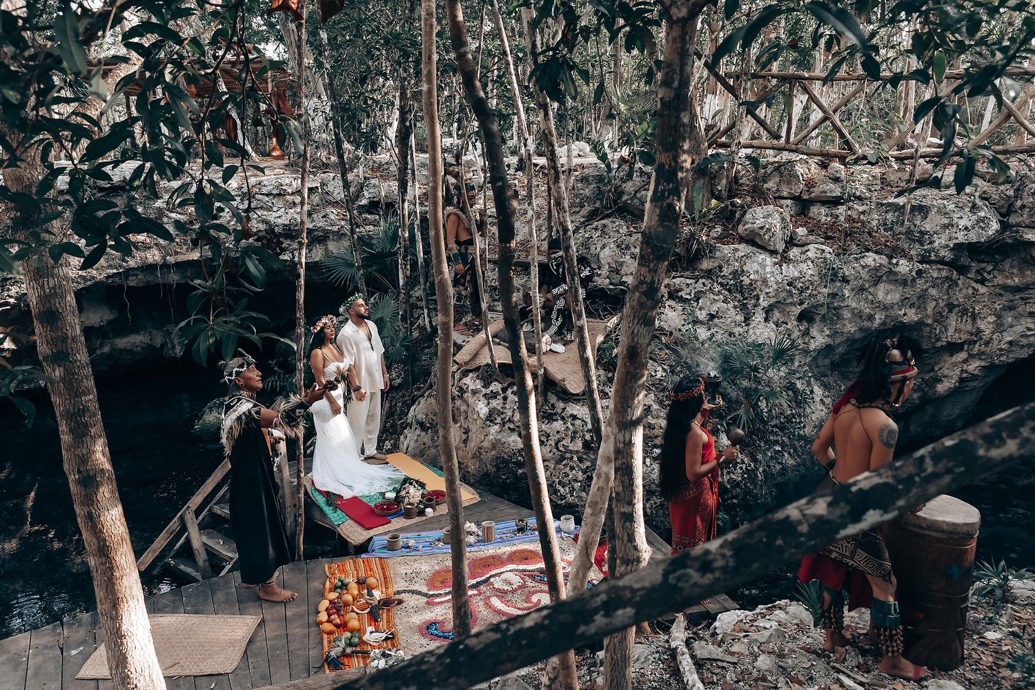 Wedding celebration in a wooded area with guests gathered around the ceremony space.