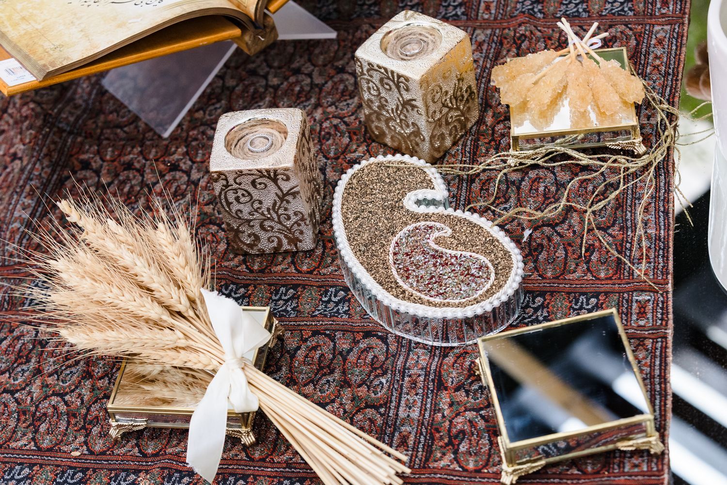 Decorative Persian rug display with ornate wooden boxes, dried wheat, seeds, and gold mirror wedding accessories.