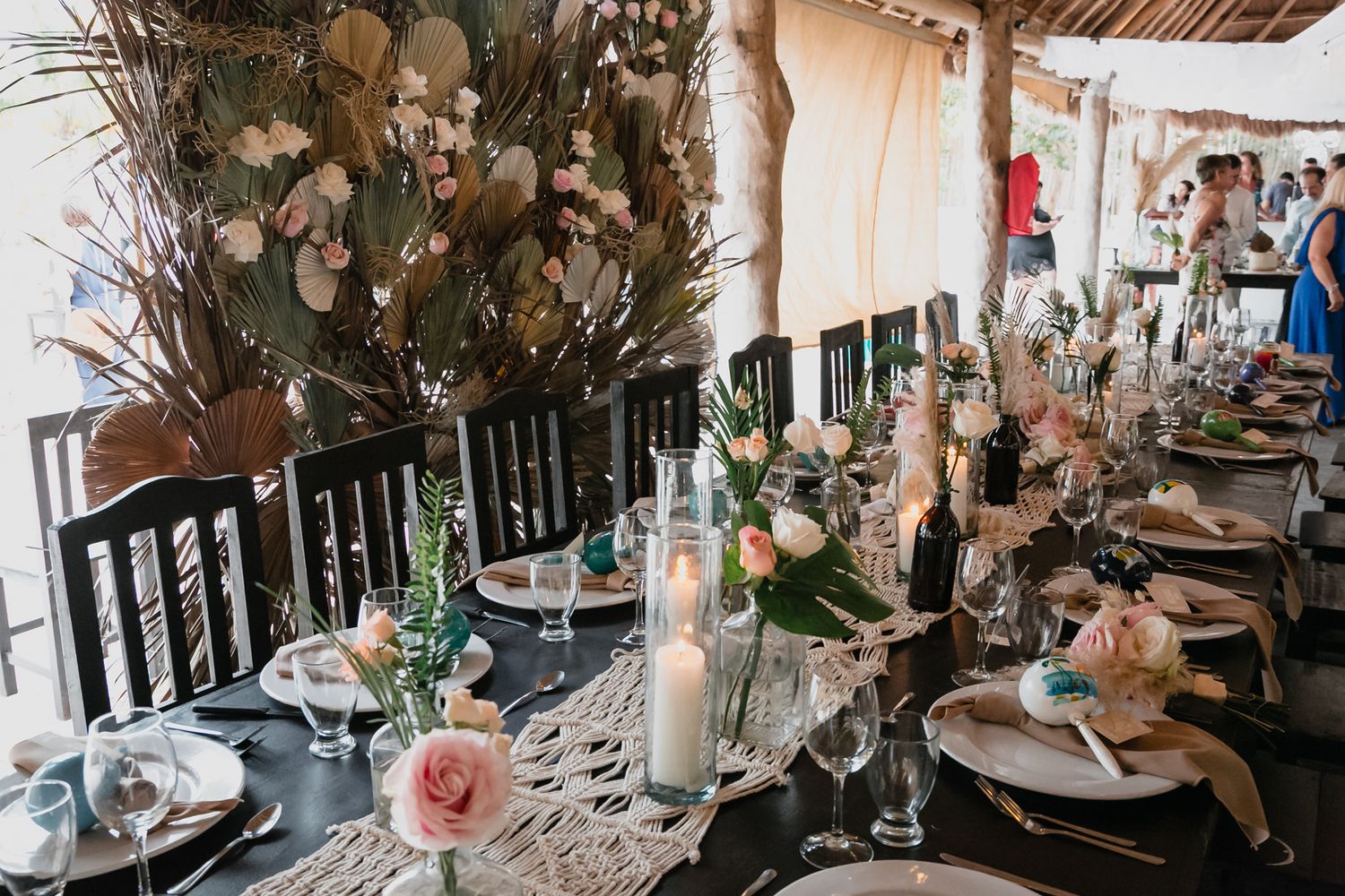 Elegant beach wedding reception table adorned with dried florals, candles, macrame runner, and pink roses.