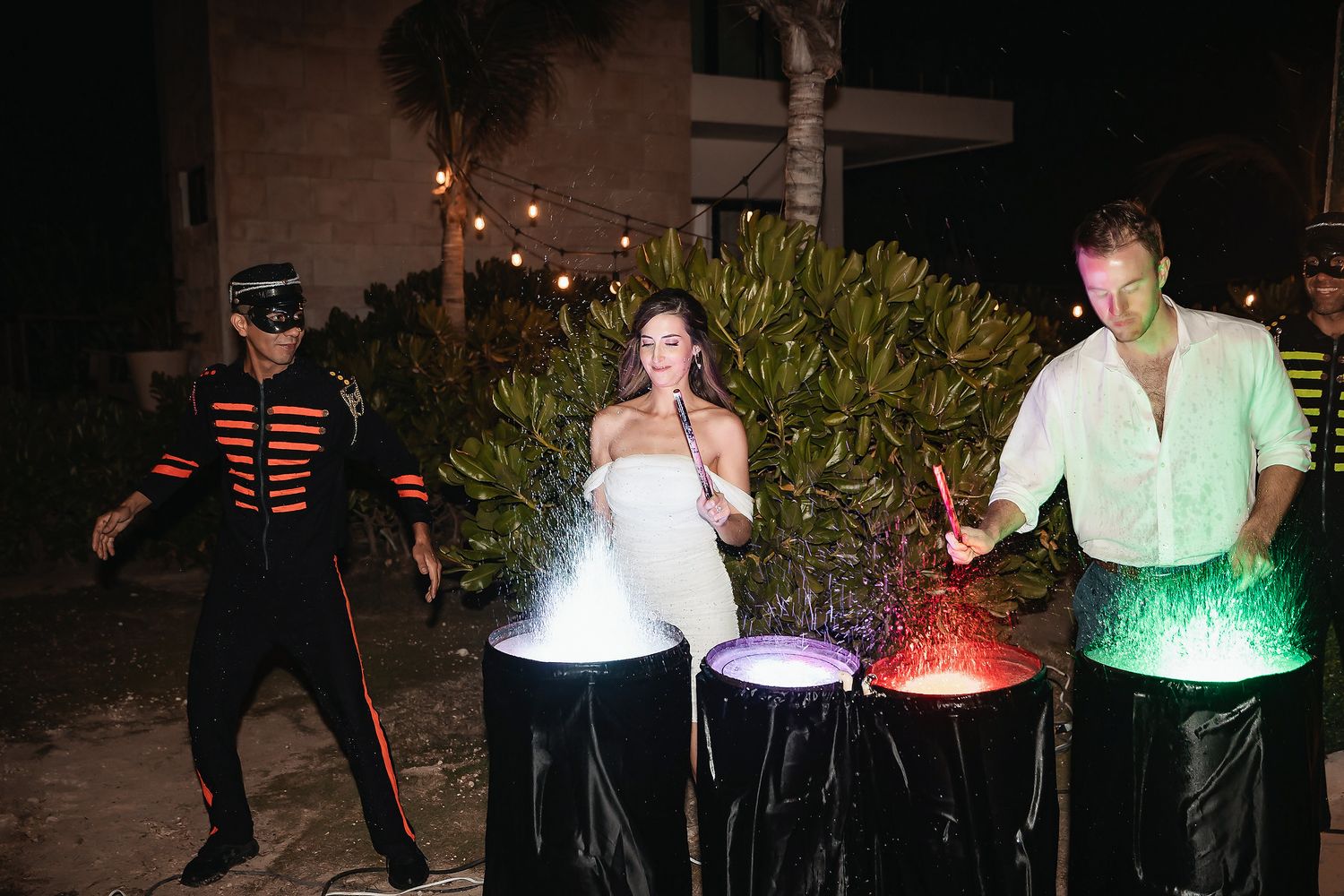 Bride and guests playing illuminated drums with colorful smoke effects at an outdoor nighttime wedding reception.
