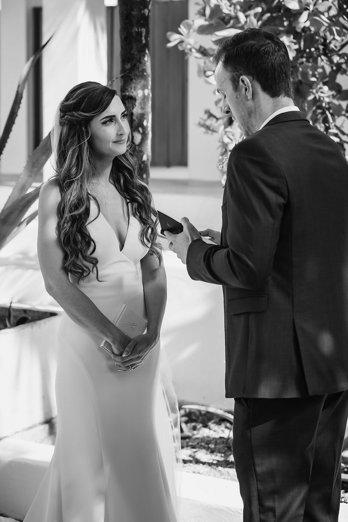 Black and white photo of a bride and groom exchanging vows during an outdoor wedding ceremony.