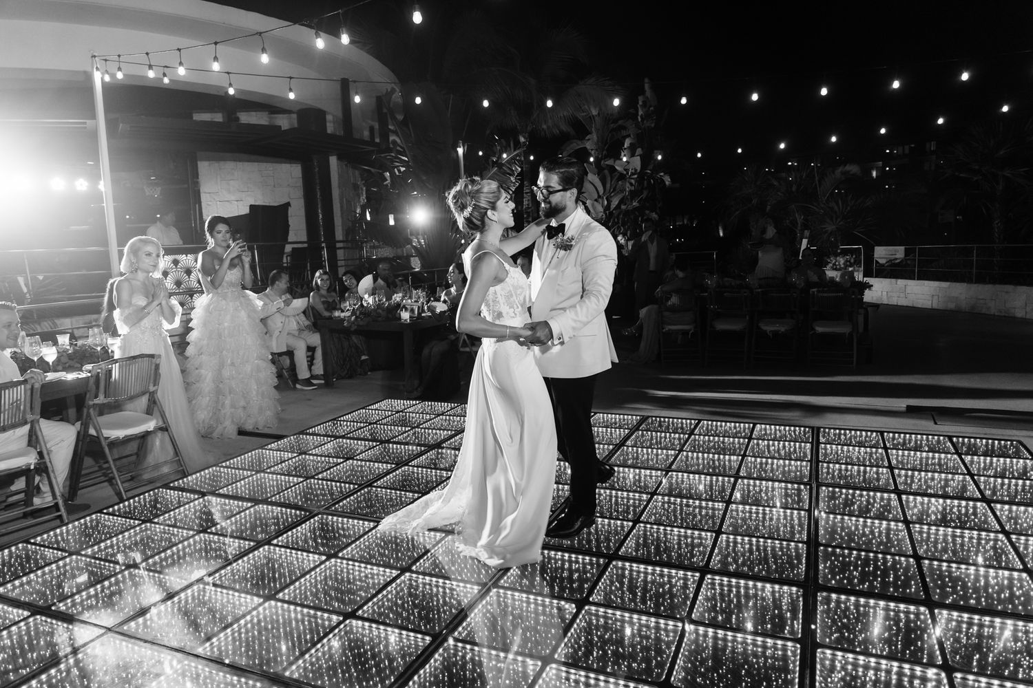 Couple shares first dance on illuminated dance floor at elegant outdoor wedding reception at night.