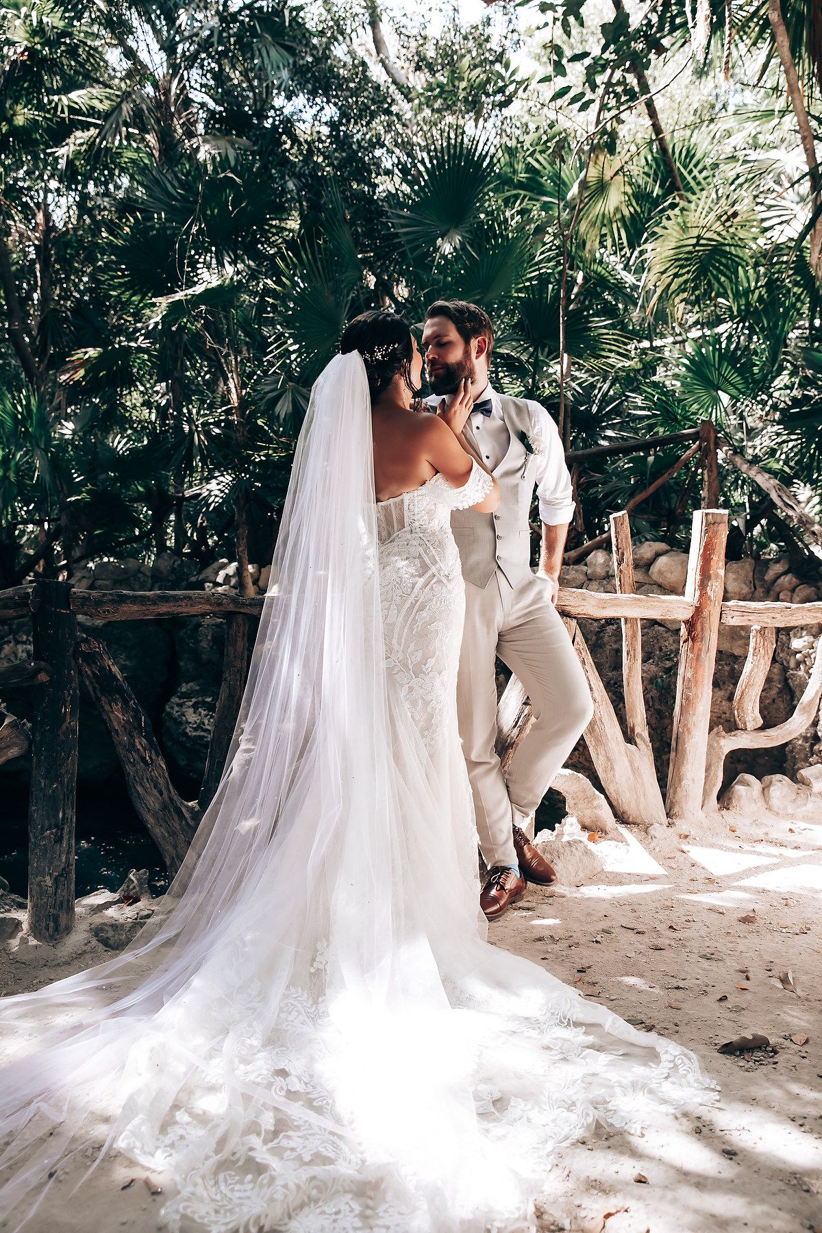 Wedding couple poses on sandy beach path surrounded by tropical foliage.