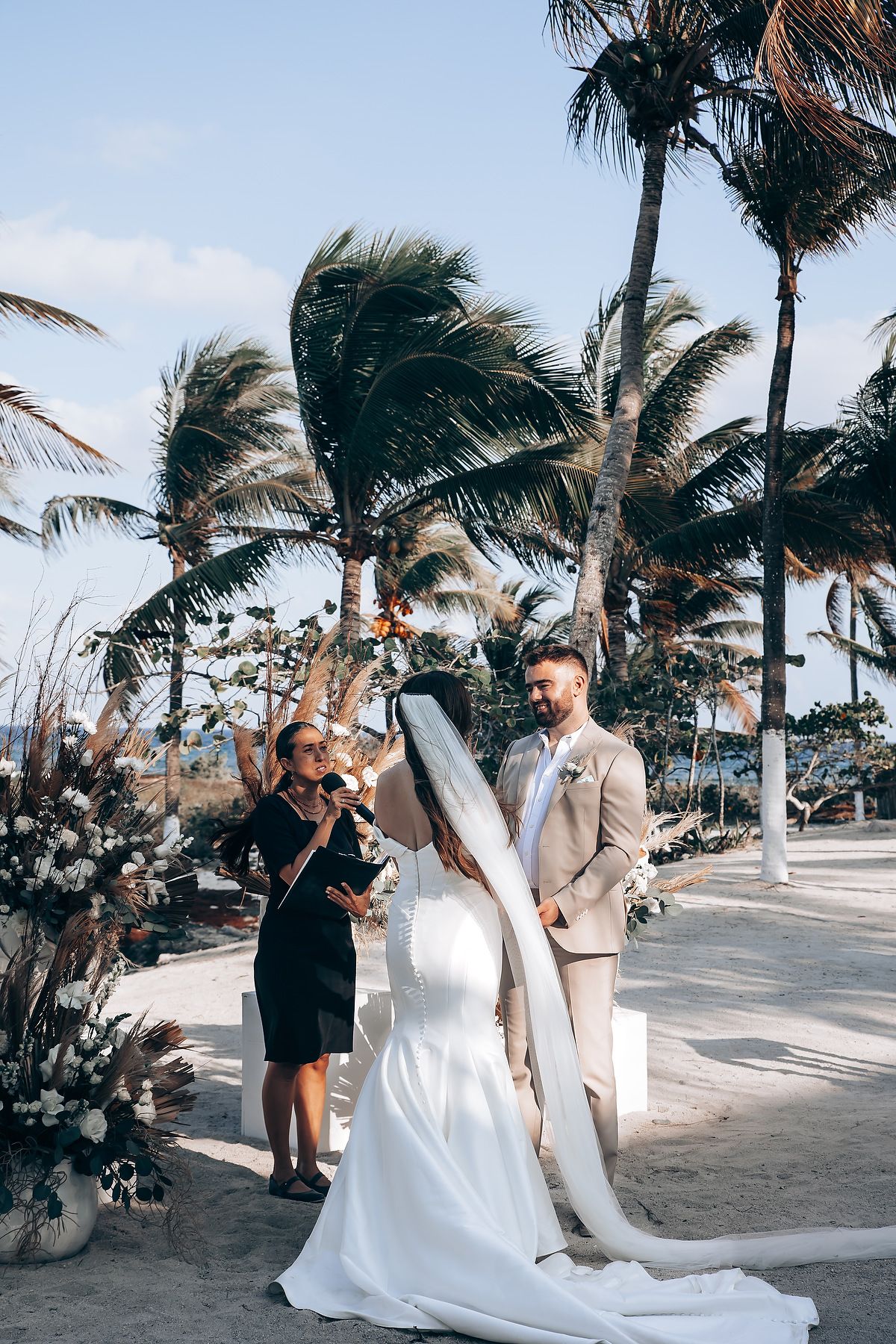Wedding party poses on a windy beach with palm trees swaying in the tropical breeze.
