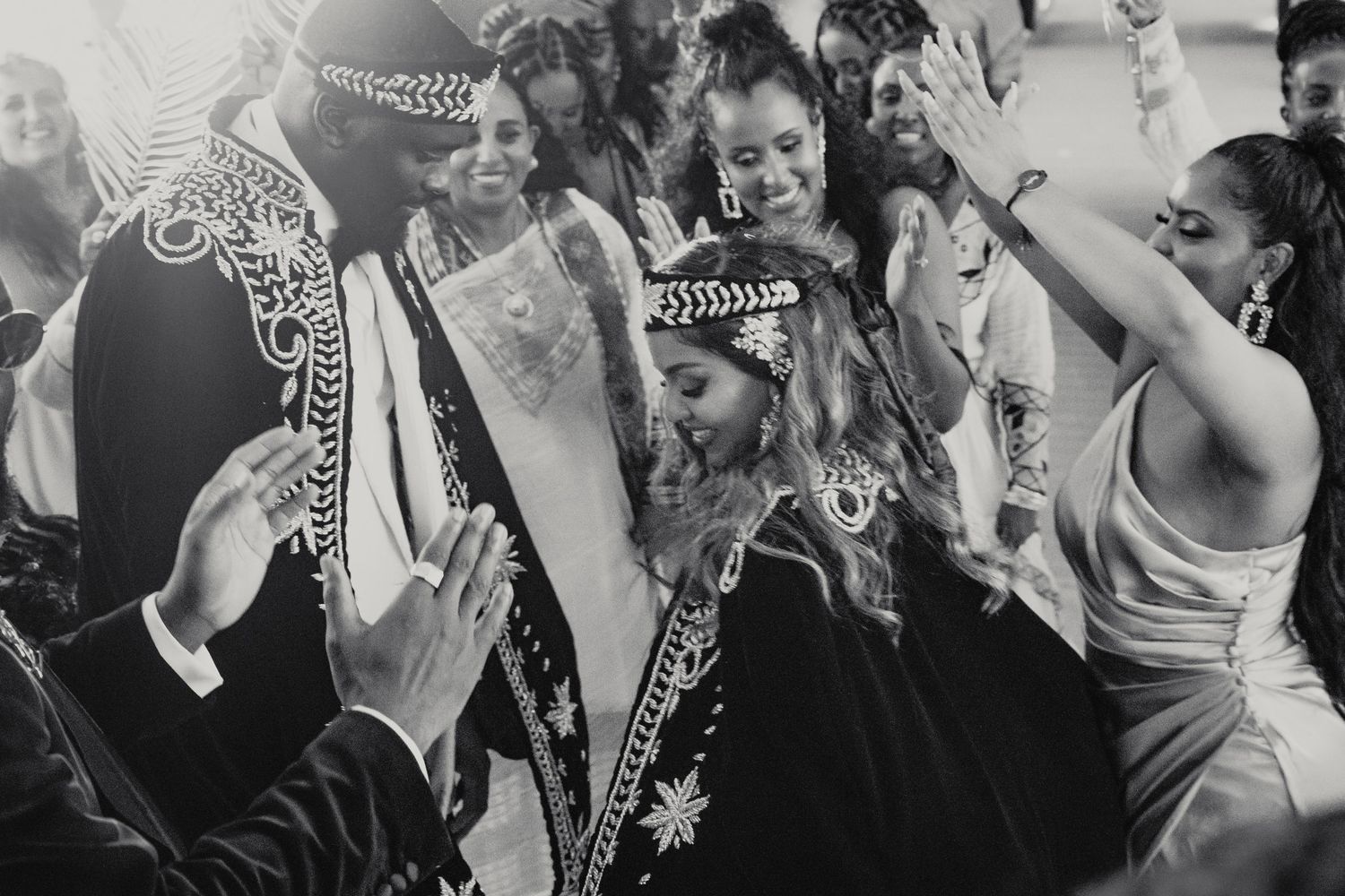 Black and white photo of joyful wedding guests celebrating with couple in traditional attire.