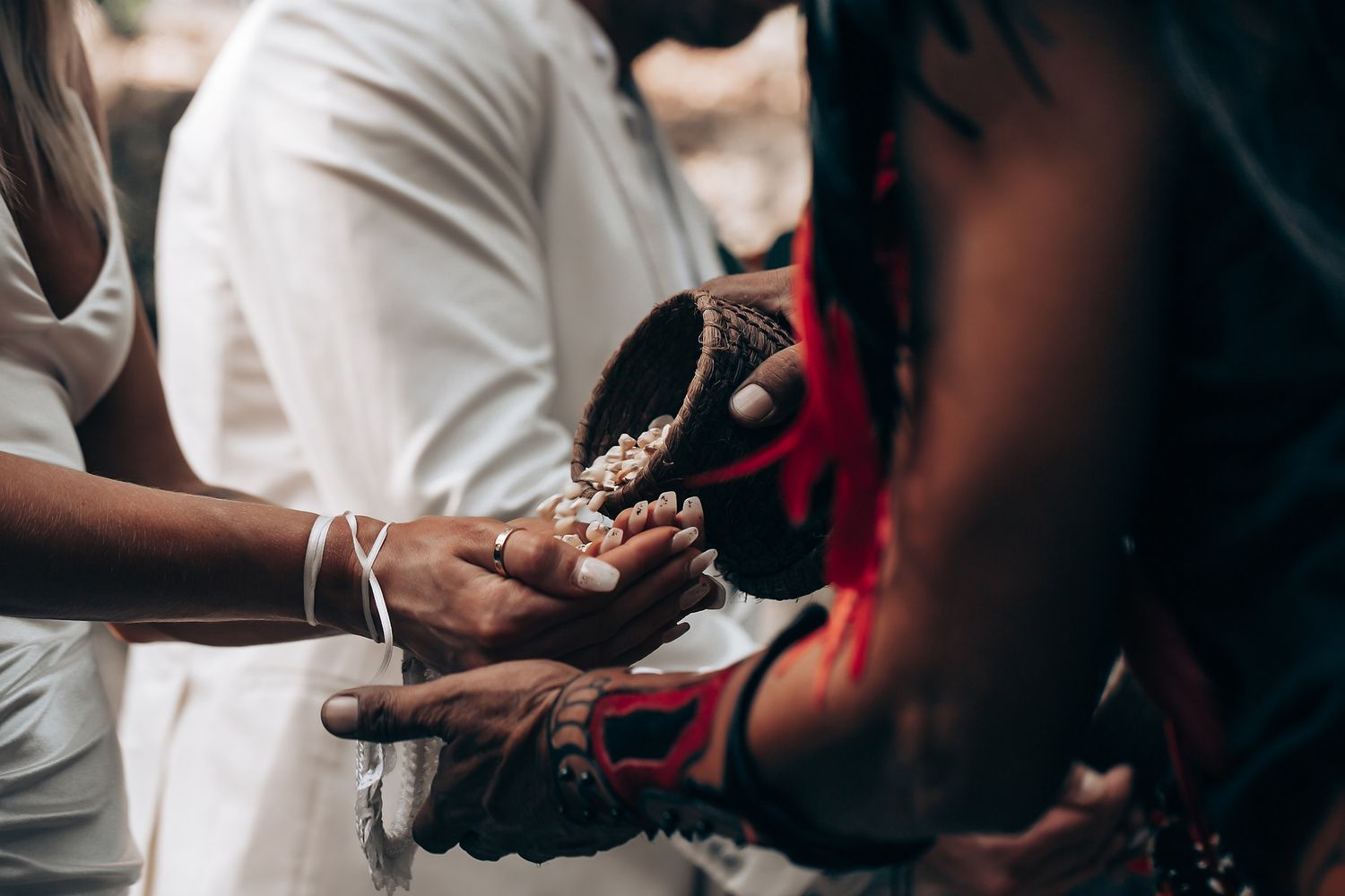 Hands performing a traditional blessing ritual with ceremonial objects and white clothing.