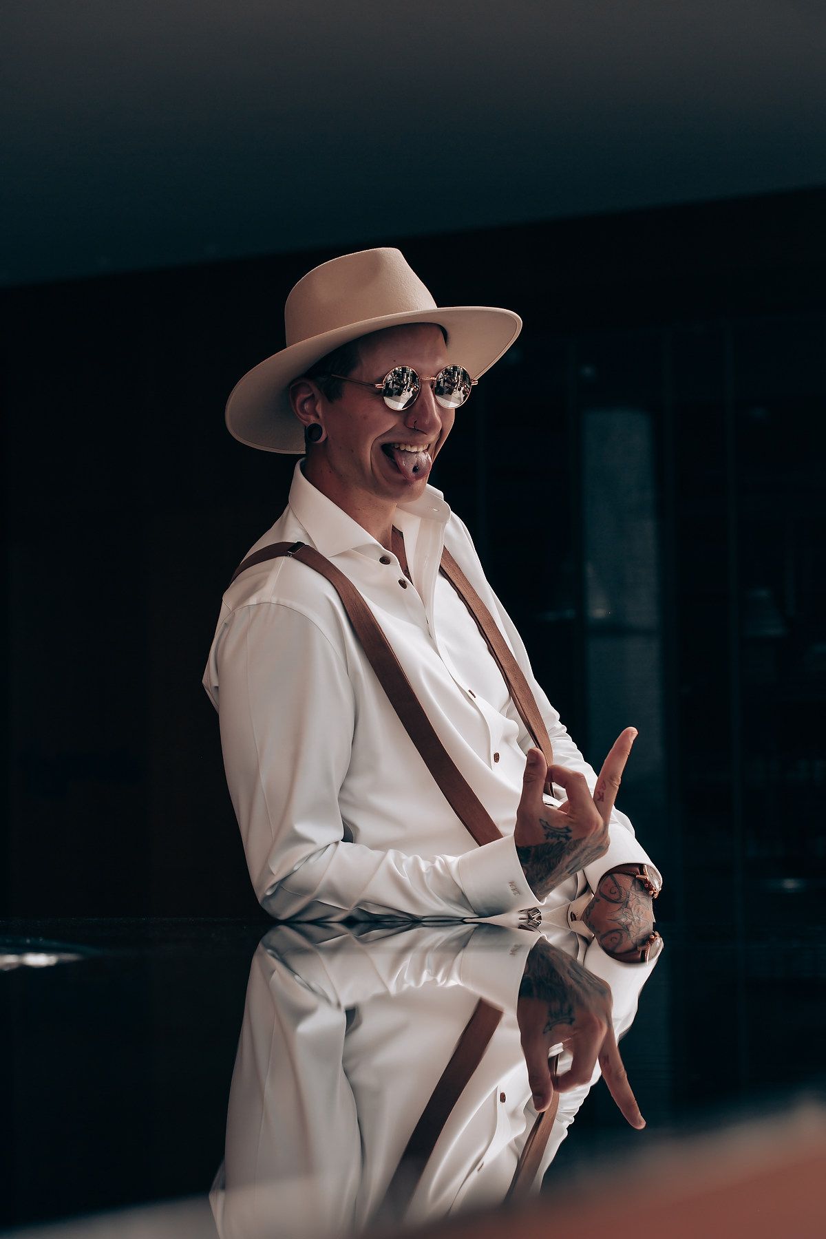 A person in a white suit and hat gestures while standing in a dark setting.