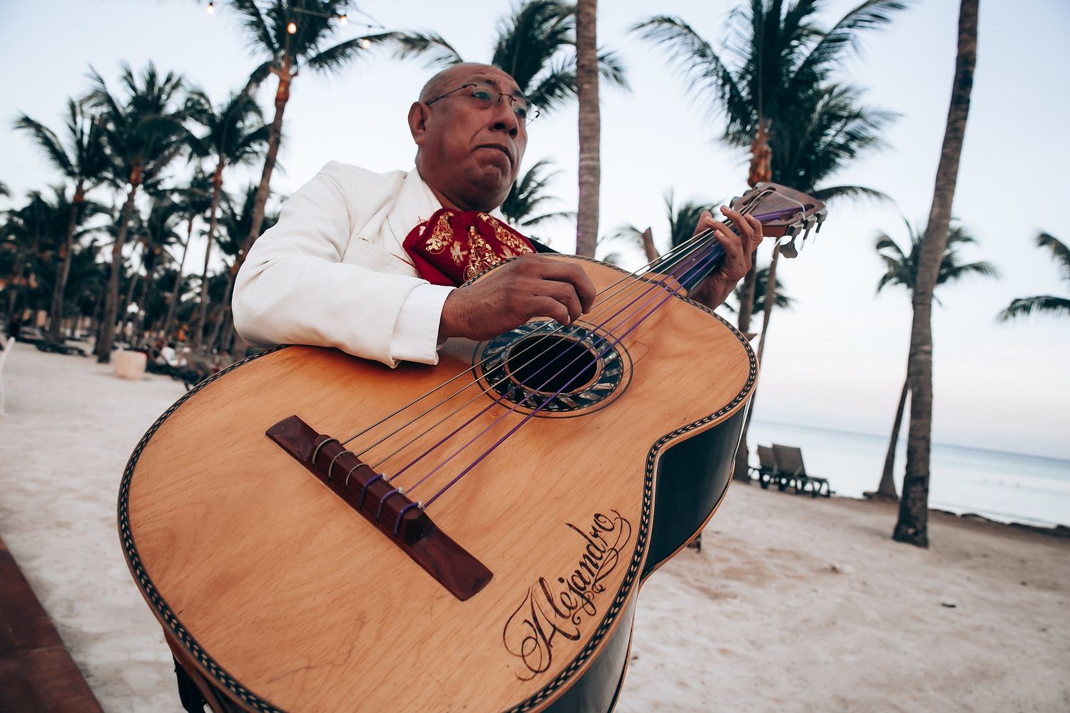 An acoustic guitar rests on sandy beach with palm trees during a tropical wedding.