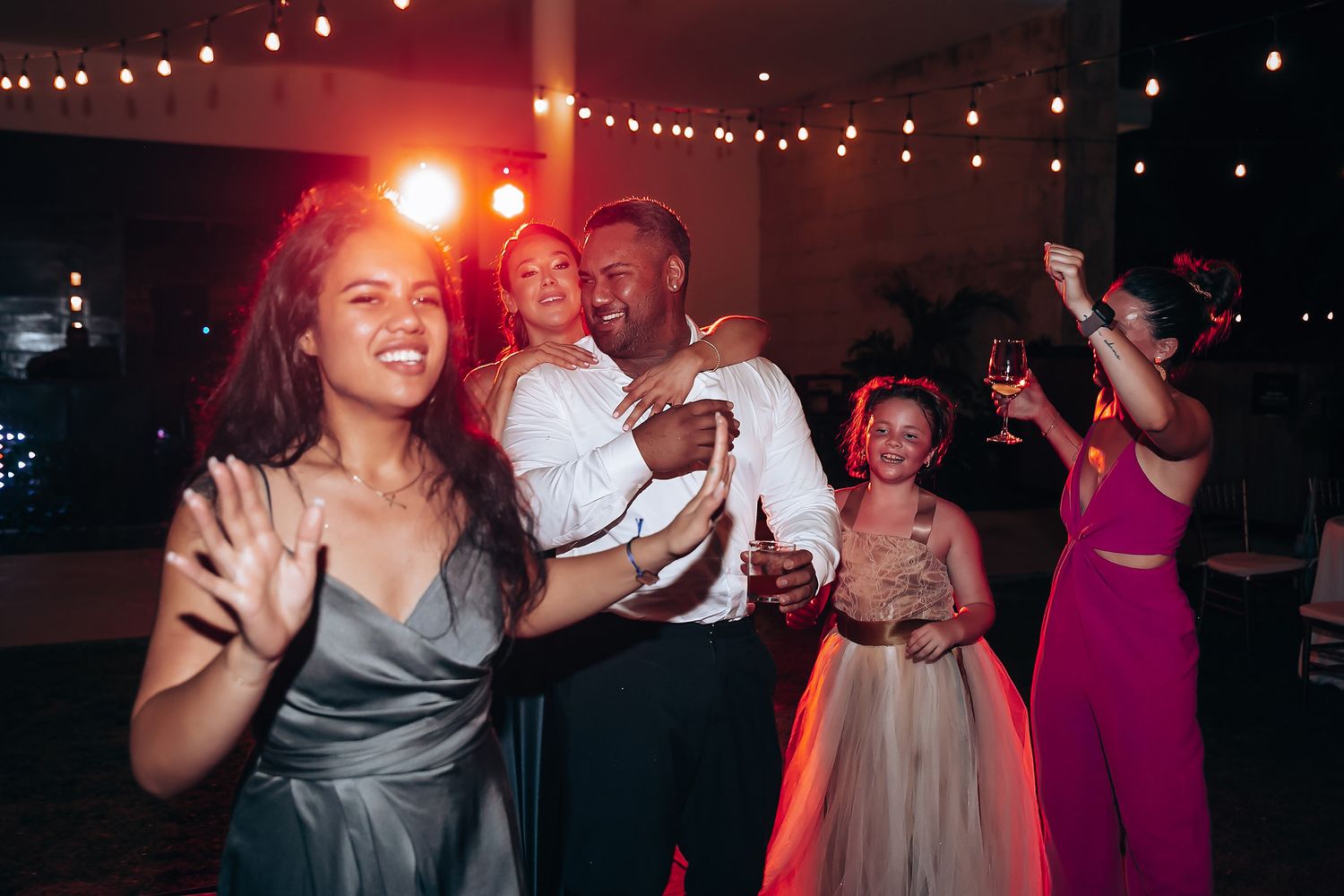 Wedding guests dancing under string lights at evening reception.