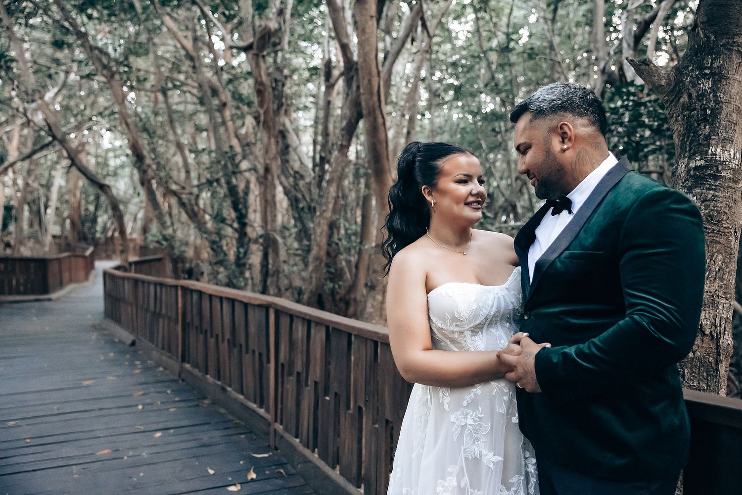 Romantic wedding couple shares intimate moments on a rustic wooden boardwalk surrounded by trees.