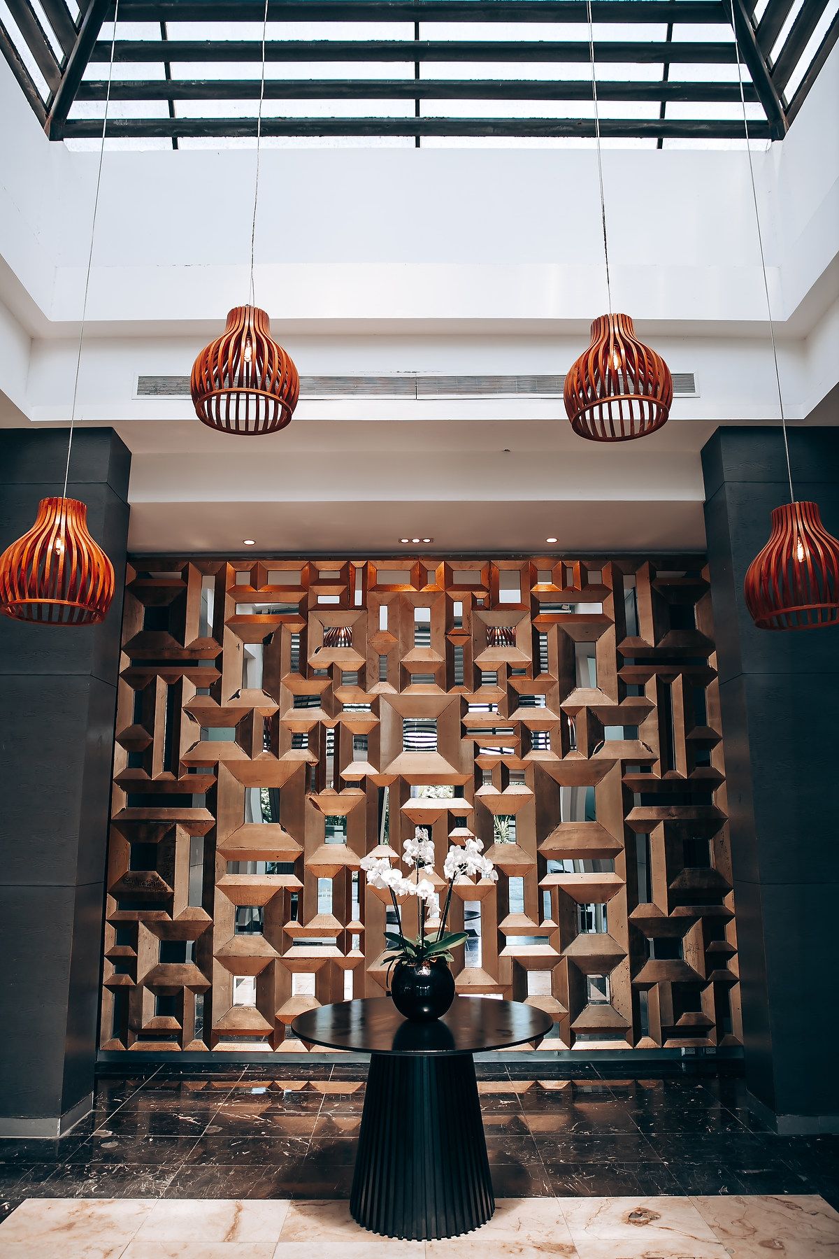 Modern interior space with geometric wall panels and orange pendant lights hanging from skylights.