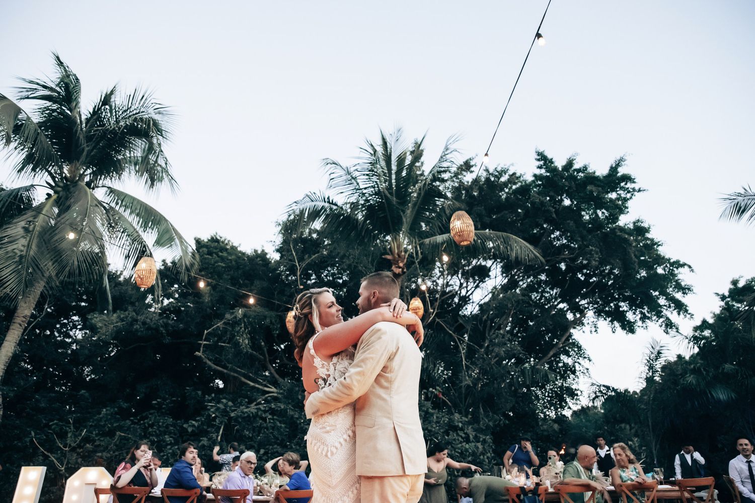 Bride and groom sharing first dance under string lights at outdoor tropical wedding.