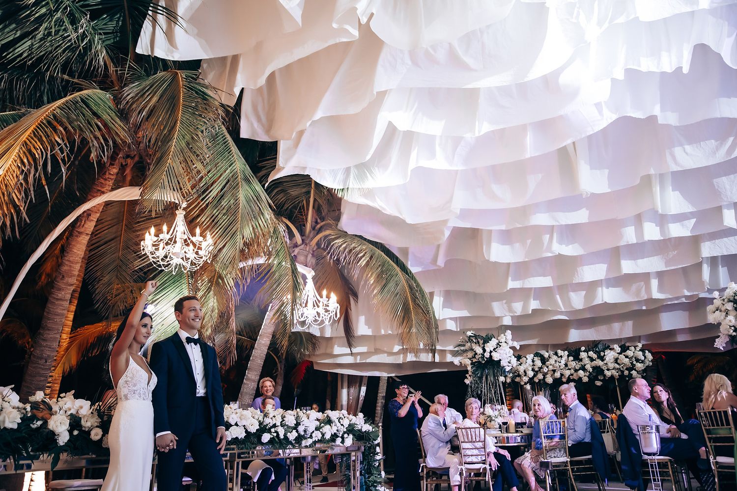 Wedding reception venue with elegant white draped ceiling and crystal chandeliers.