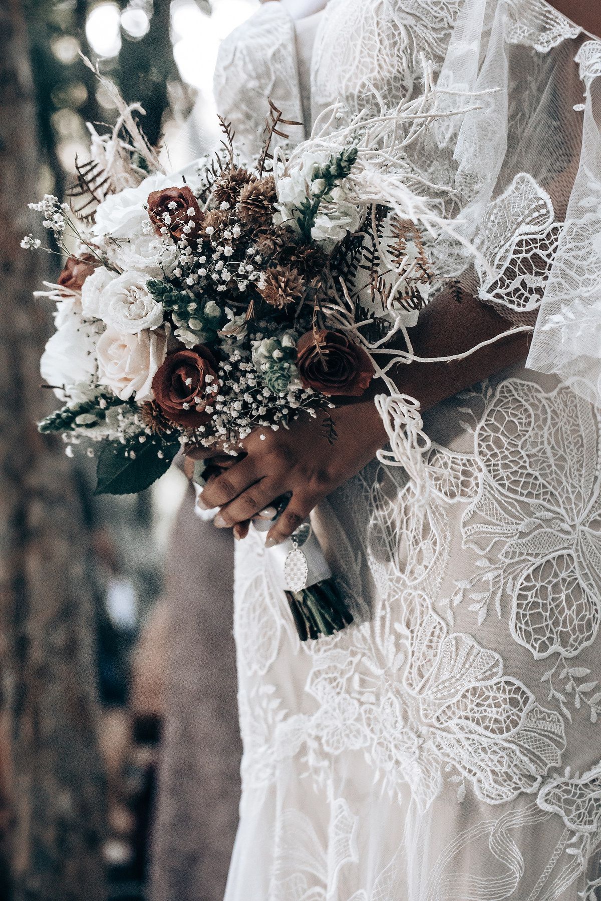 A delicate bridal bouquet features white roses, baby's breath and lace details against a wedding dress.