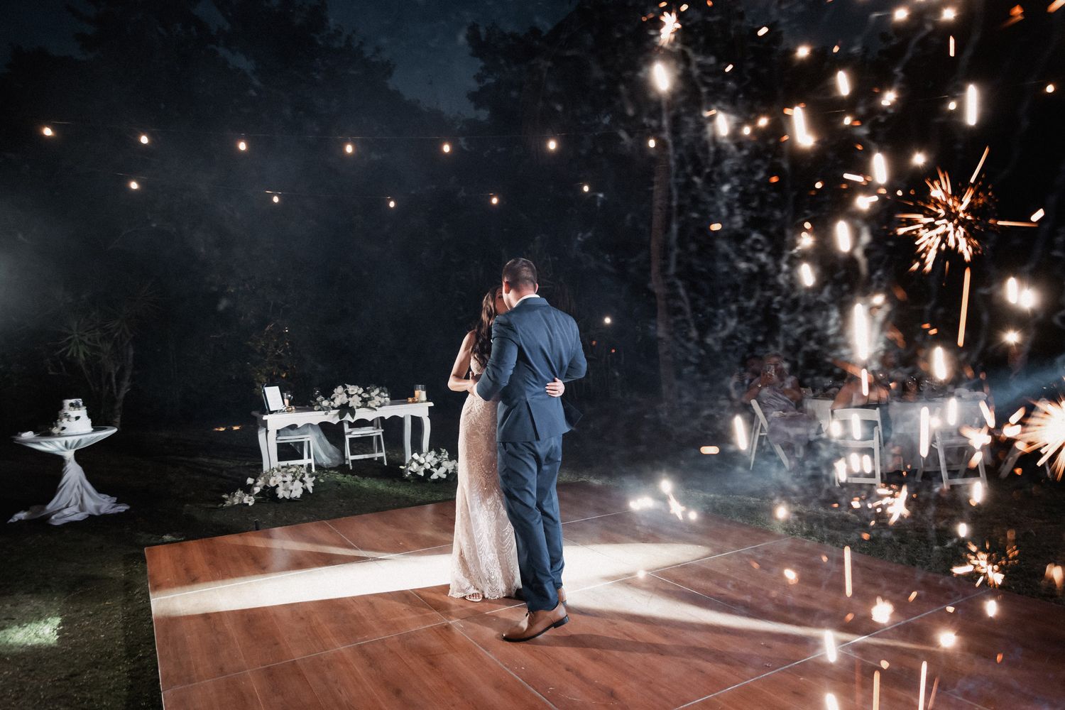 Couple shares romantic first dance with sparklers illuminating the outdoor night reception.