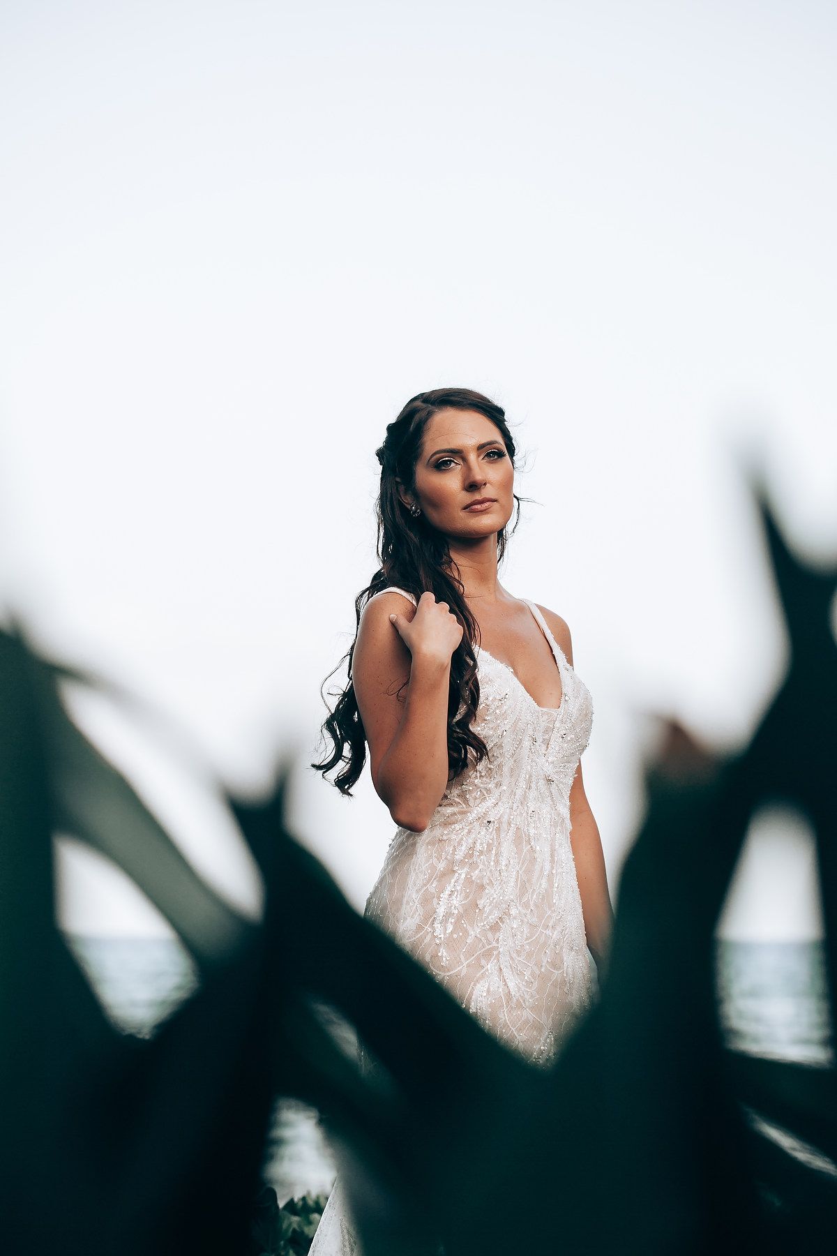Artistic bridal portrait with silhouetted leaves in foreground creating dramatic framing.