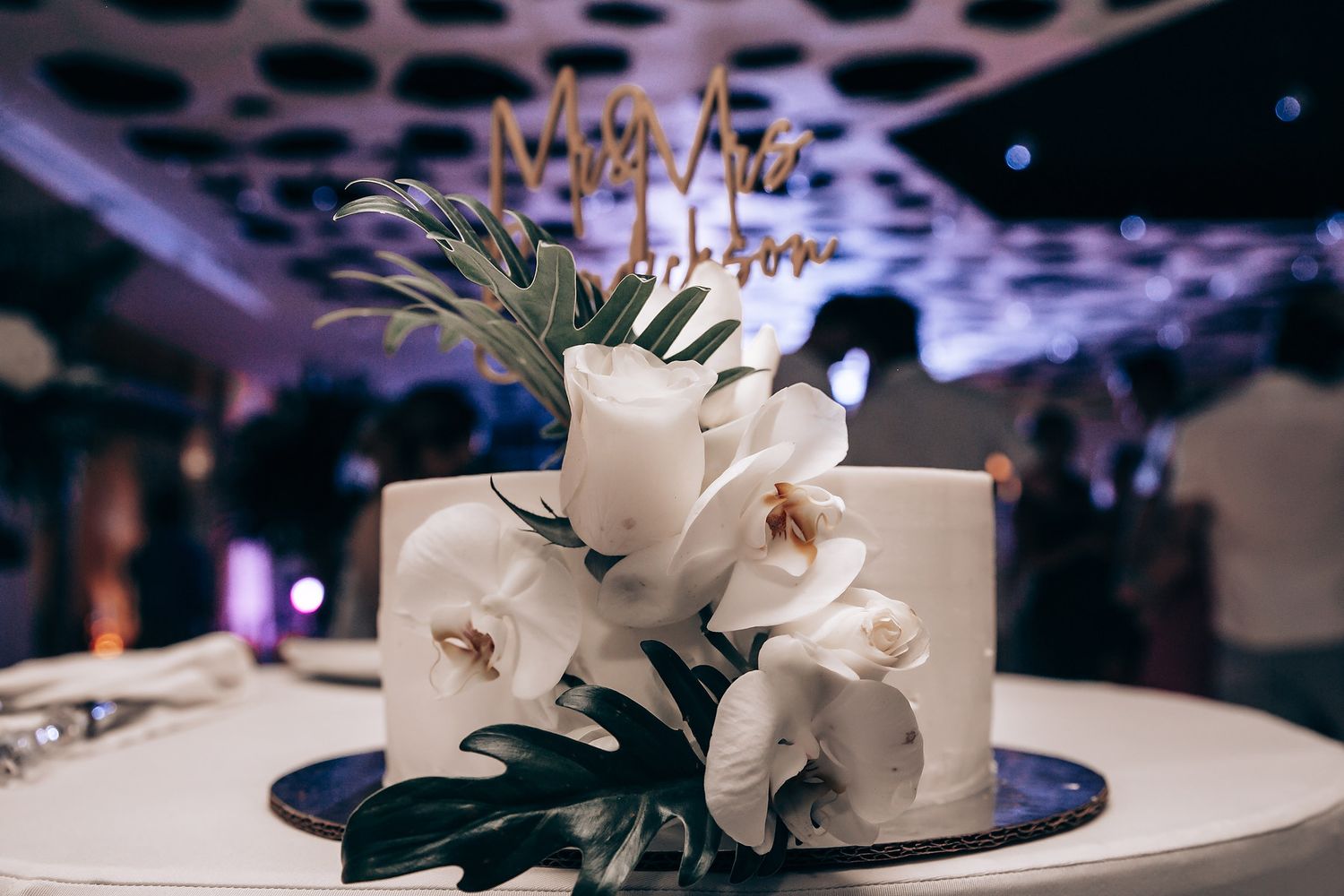 White orchid centerpiece arrangement on a dark table at an elegant reception.