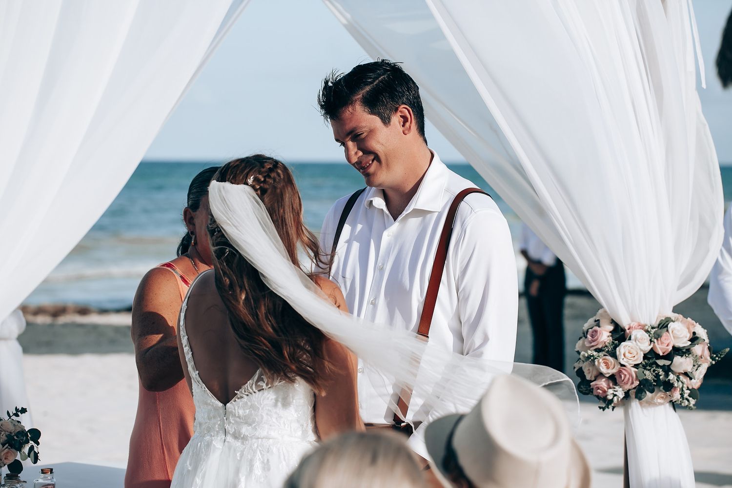Elegant beach wedding setup with white draped canopy and floral arrangements by the ocean.