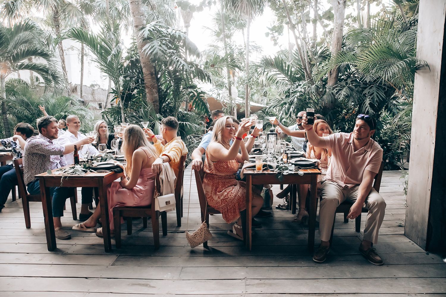 Wedding reception guests dining at outdoor tables surrounded by palm trees and tropical landscaping.