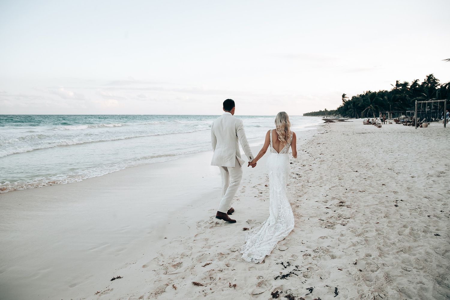 Couple walking along pristine white sand beach in wedding attire.
