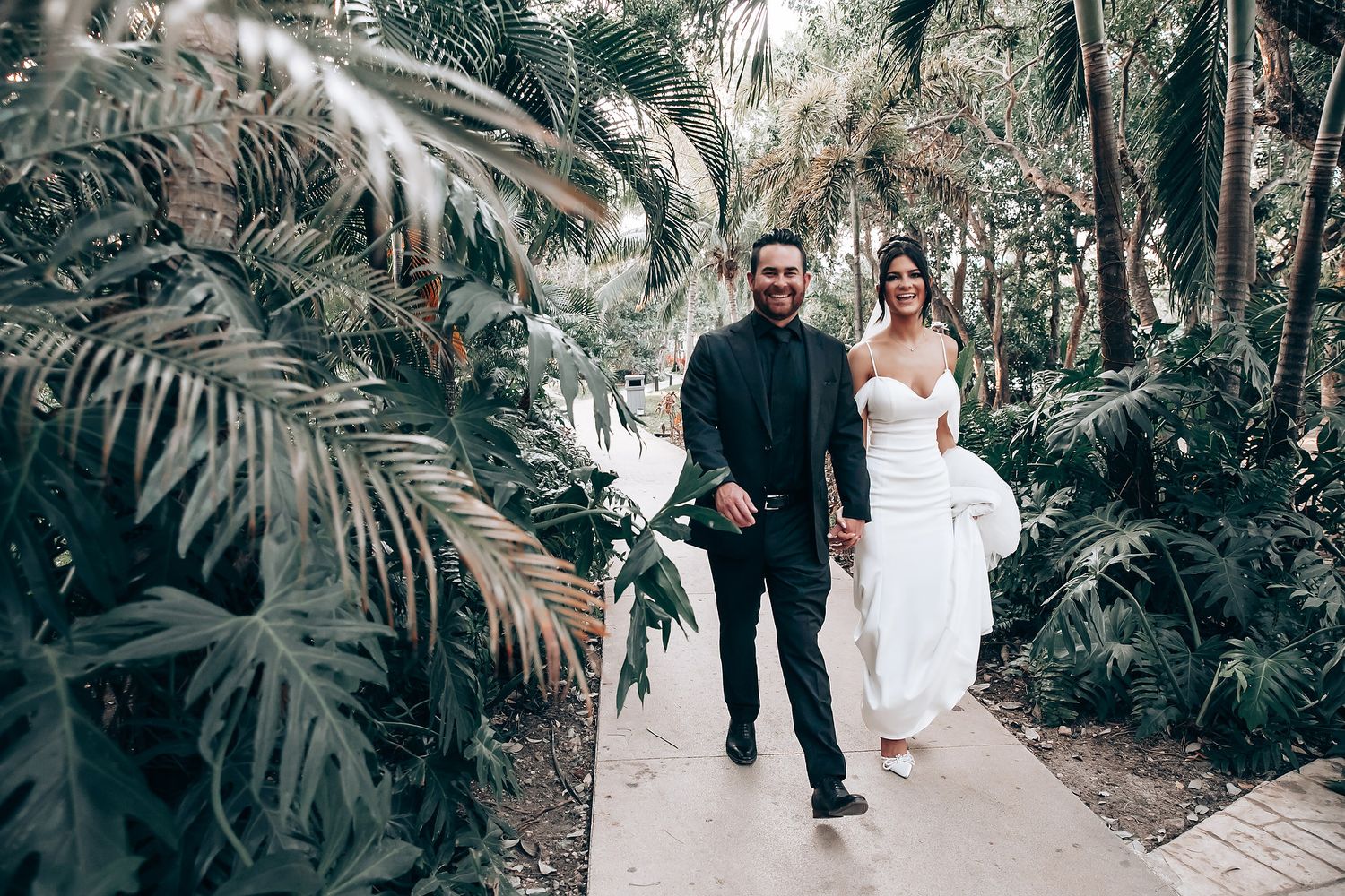 A couple walks along a tropical garden path lined with palm trees and lush greenery.
