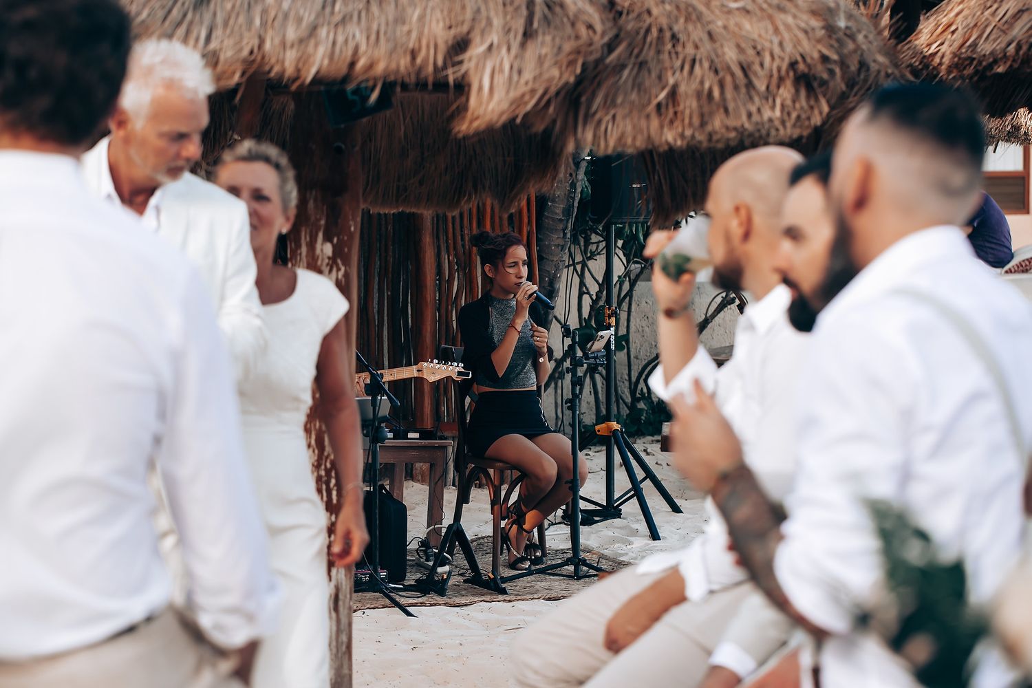 Guests enjoying a festive celebration under thatched umbrellas at a tropical beach venue.