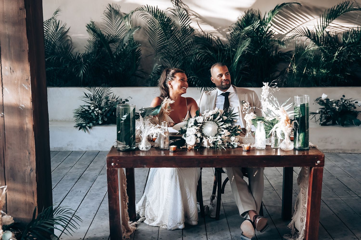Wedding reception setup with wooden tables and tropical decor in an outdoor setting.