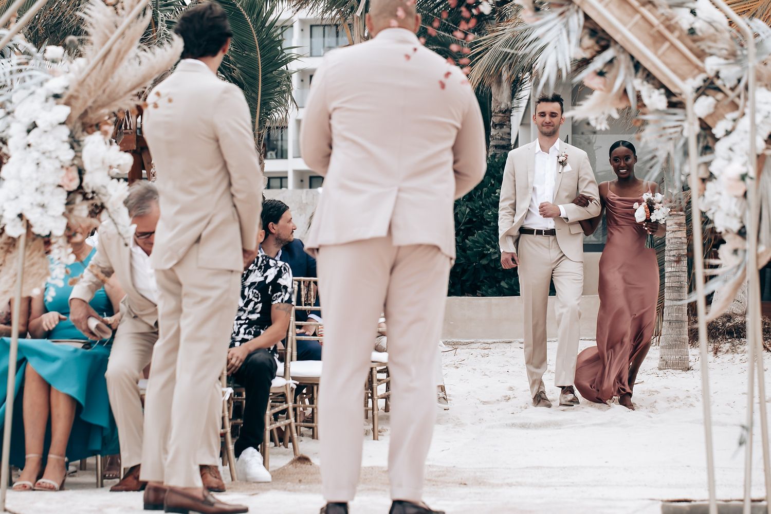 Wedding guests in light beige and neutral attire gathered on a sunny beach.