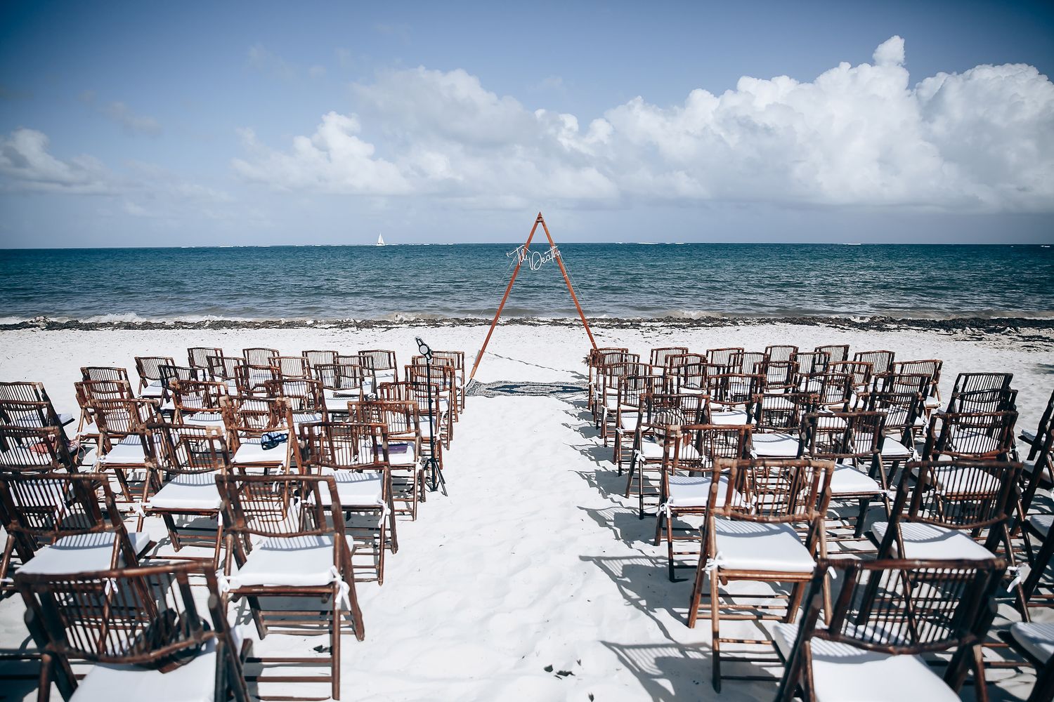Wooden chairs set up on a white sandy beach for an oceanfront wedding ceremony.