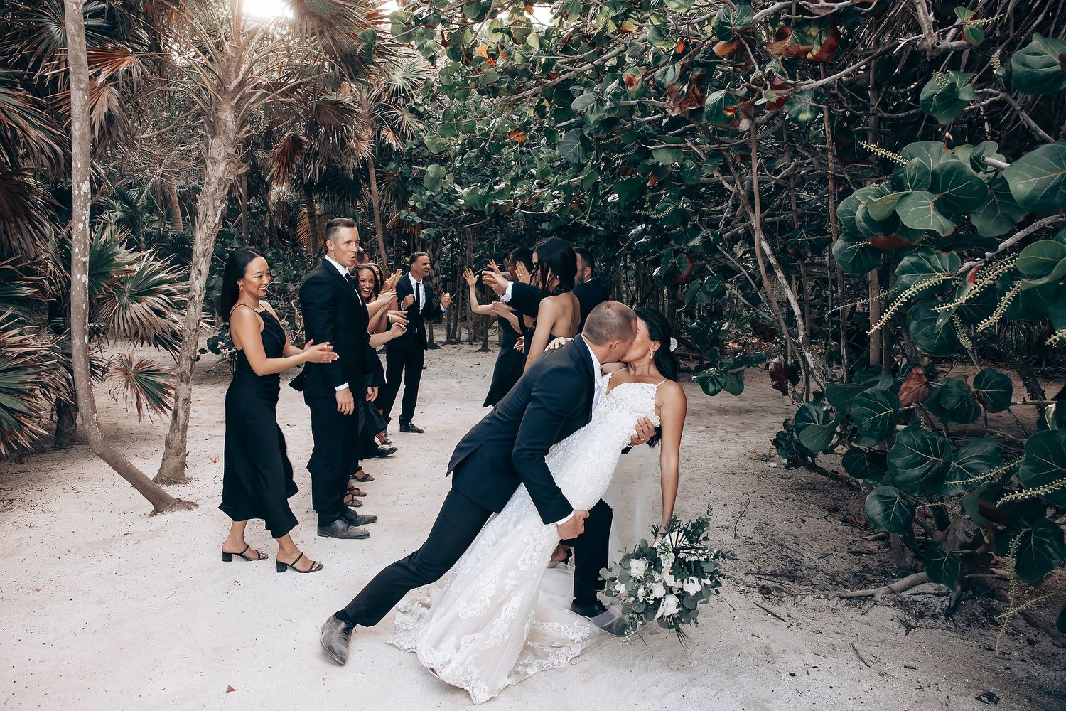 Wedding party poses along tropical beach path with natural sunlight.