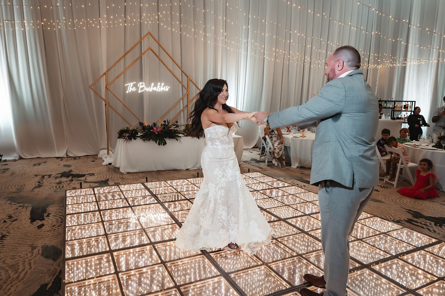 Bride and groom share their first dance on a glowing white LED dance floor at an elegant wedding reception.