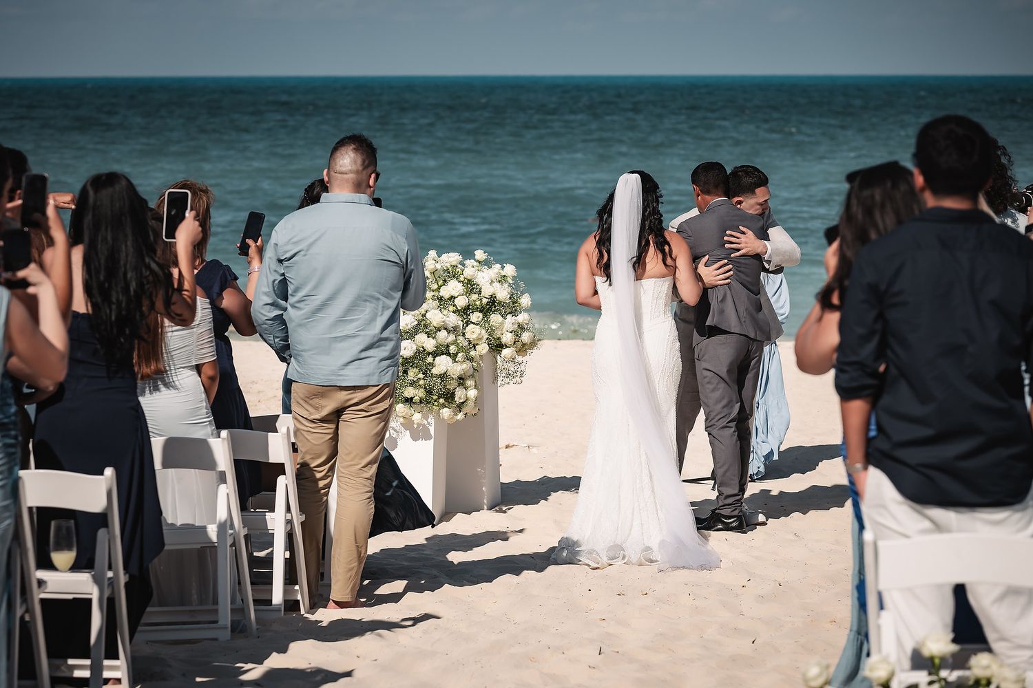 Bride and groom exchanging vows at a romantic beach wedding ceremony with ocean views and white floral arrangements.