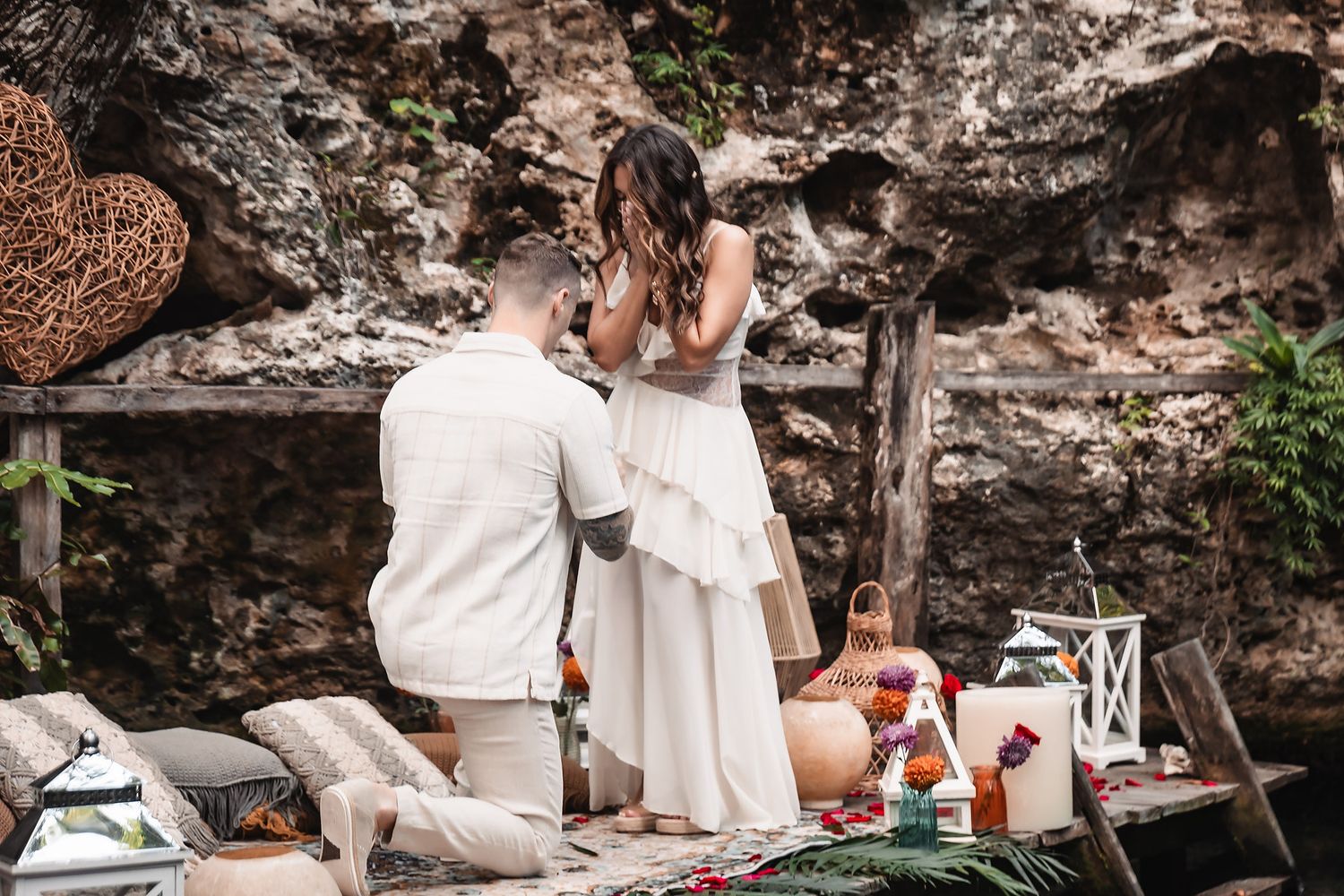 Romantic proposal moment captured on decorated platform with white lanterns and rose petals.