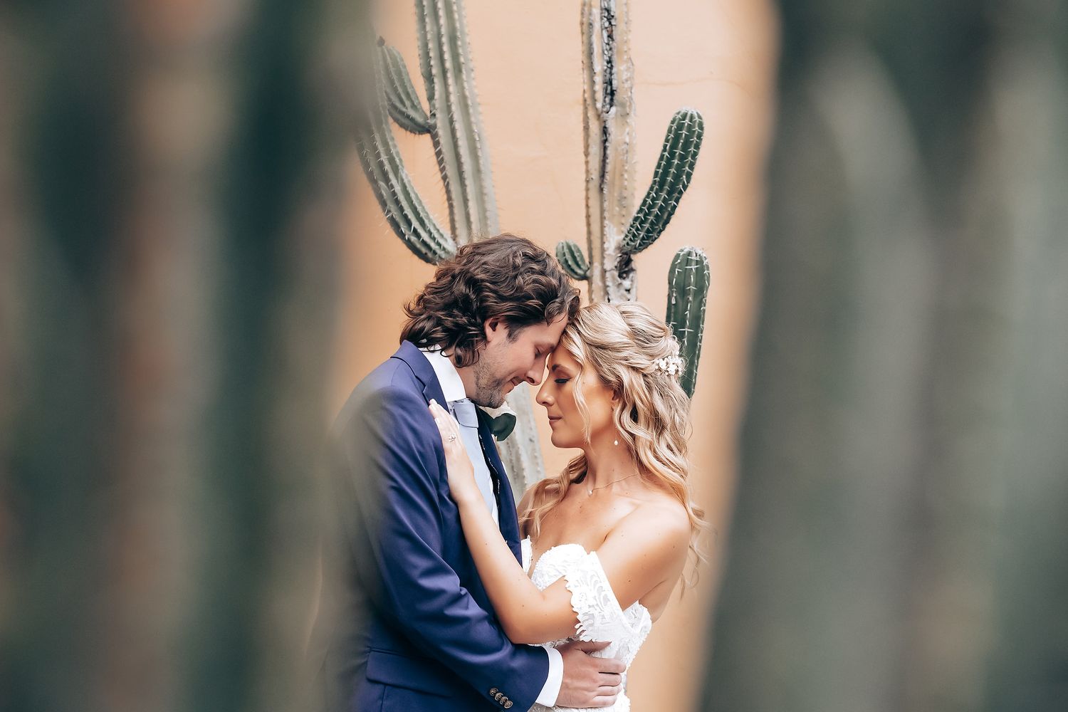 Romantic wedding couple embraces among tall palm trees at tropical venue.