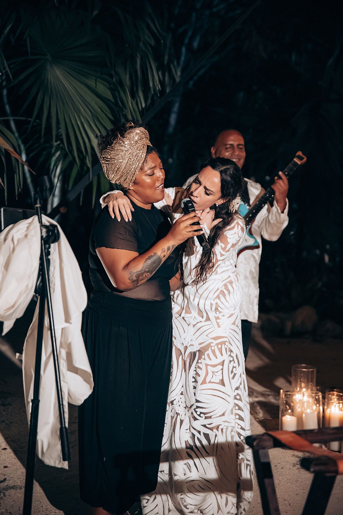 A romantic couple dances together at a nighttime outdoor celebration with palm trees and candlelight.