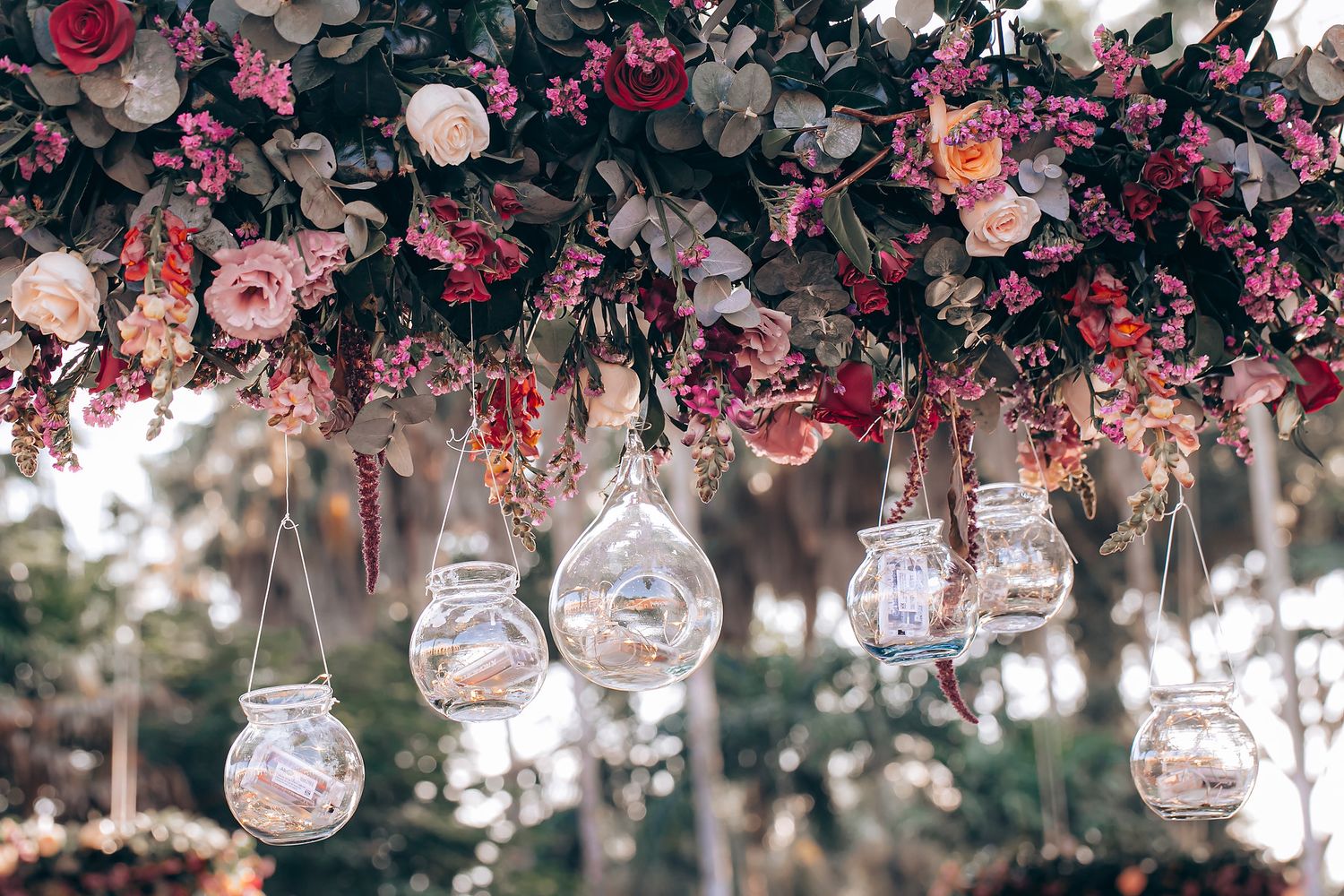 Glass orb decorations hang from pink floral branches creating a romantic garden wedding atmosphere.