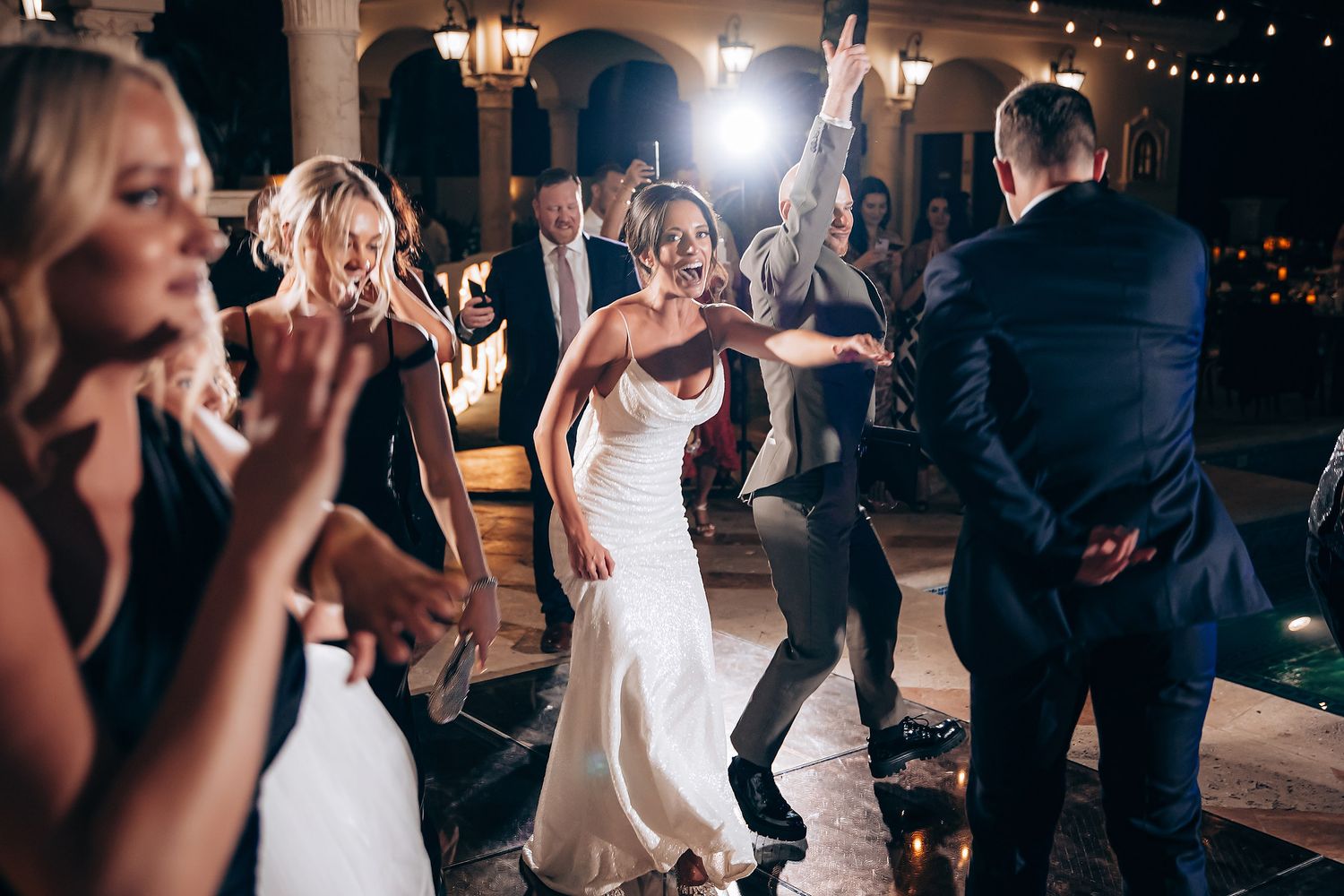 Wedding guests dance and celebrate on a dimly lit dance floor during an evening reception celebration.