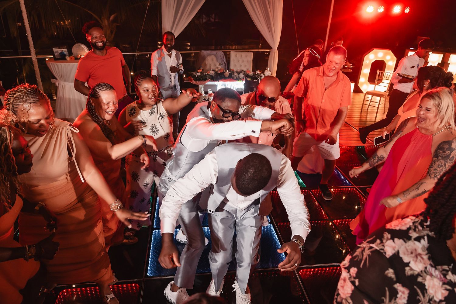 Wedding guests dance and celebrate on an illuminated dance floor during the evening reception.