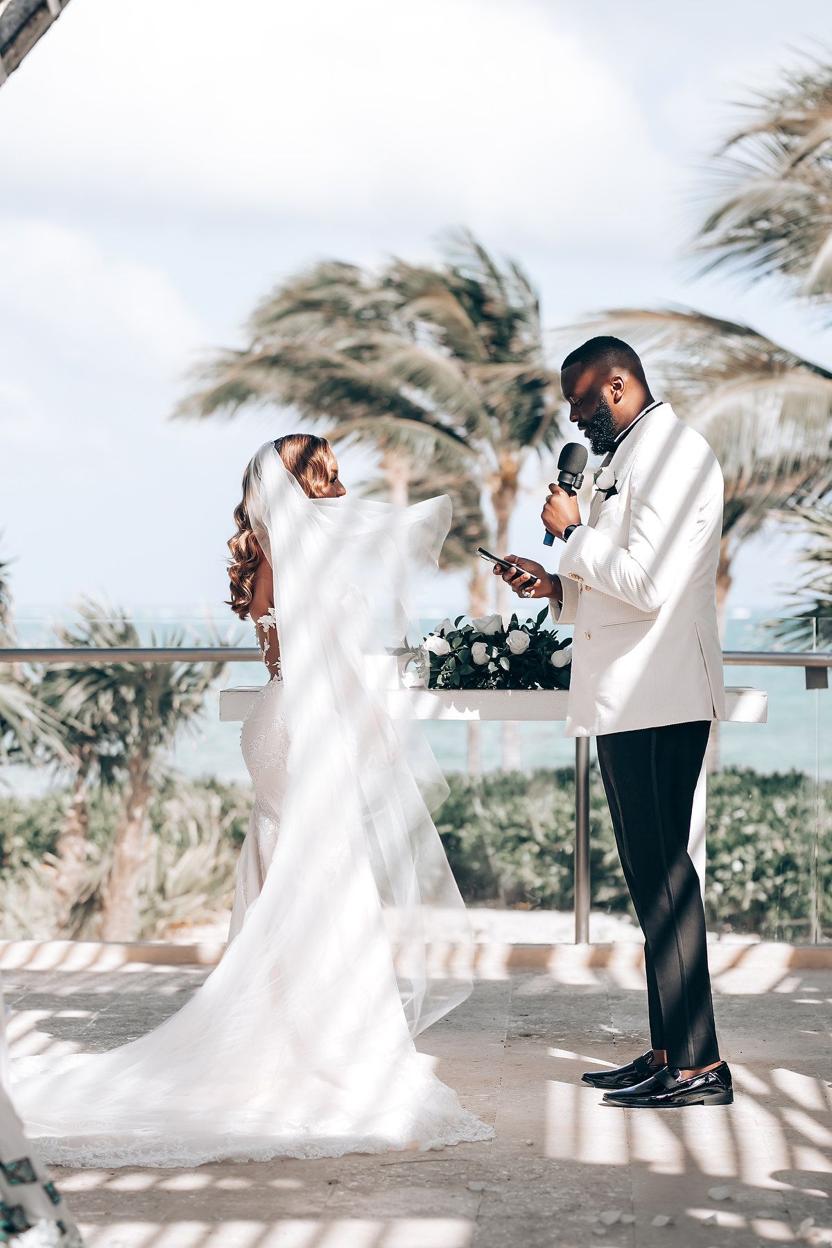 A couple poses for romantic wedding photos on a breezy beach with palm trees in the background.
