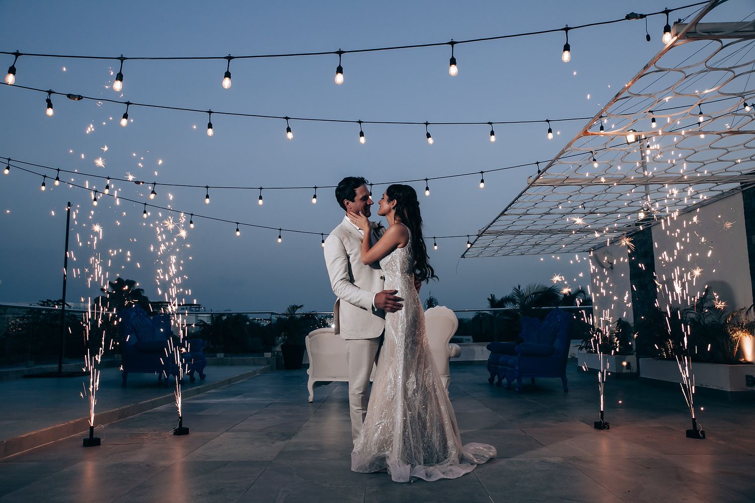 Romantic evening wedding portrait with sparkler fountains and string lights creating magical ambiance.