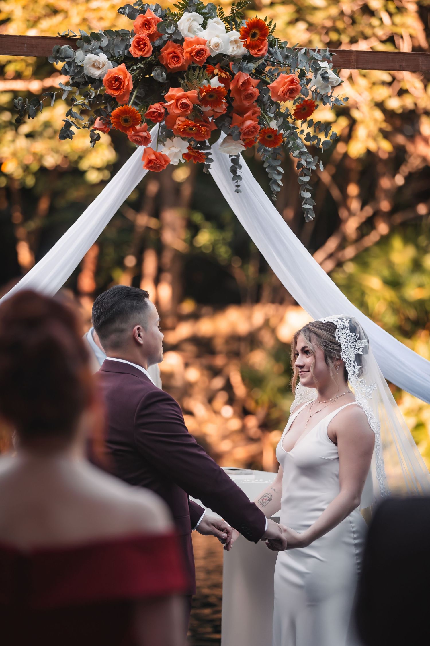Wedding arch decorated with red roses and white fabric during golden hour ceremony.