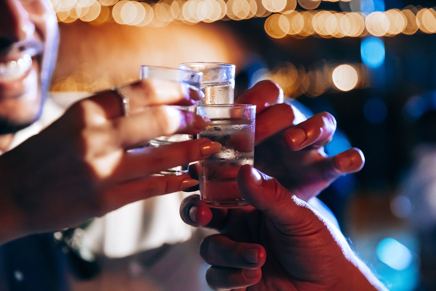 Close-up of hands toasting with shot glasses at wedding reception.