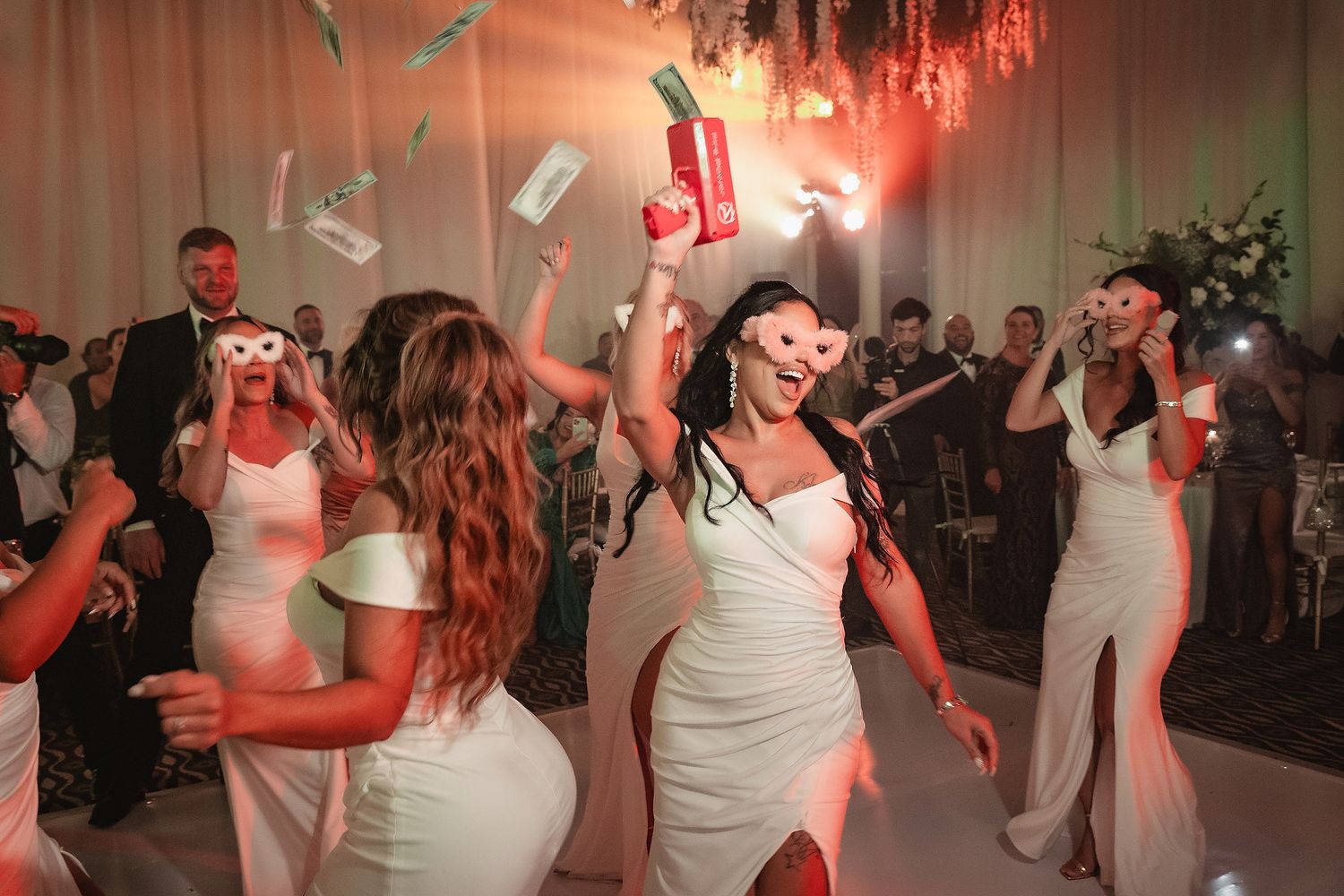 Wedding reception dance party with guests in white dresses dancing energetically under red lighting.