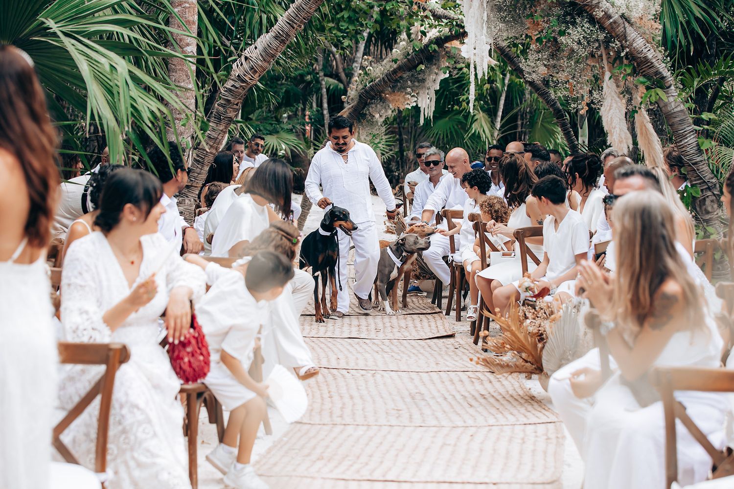 Wedding guests in all-white attire celebrating at an outdoor reception under palm trees.