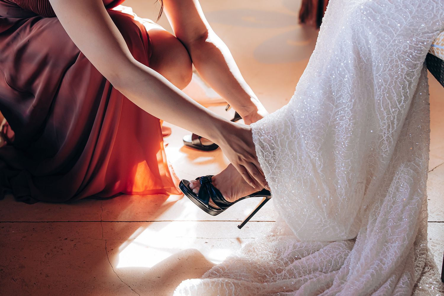 Elegant white lace wedding dress being adjusted in a warmly lit room with wooden shutters.