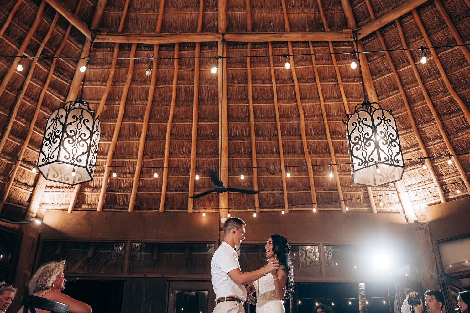 Rustic thatched roof venue decorated with hanging string lights for an evening celebration.