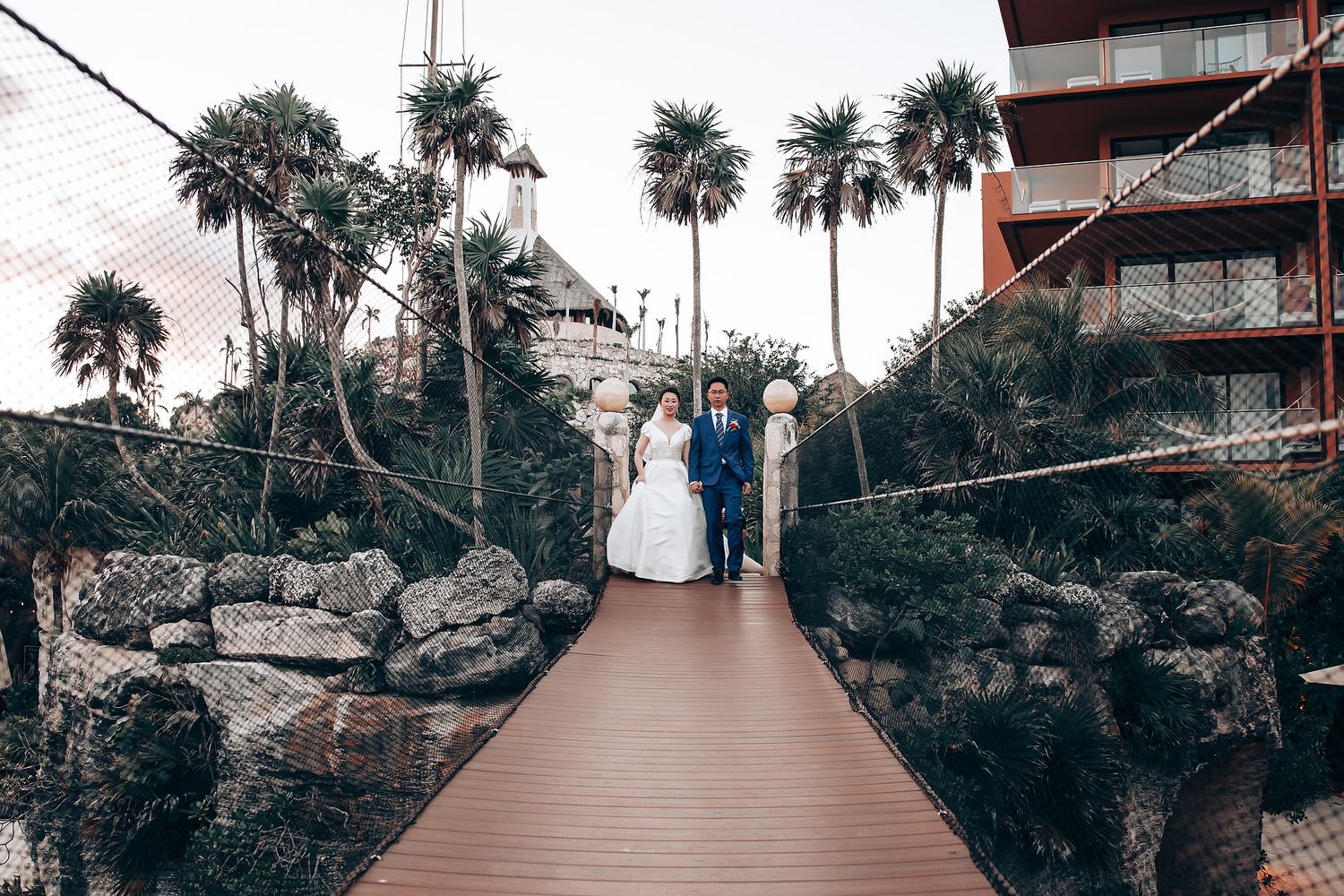 Wedding aisle decorated with palm trees and flowers leading to oceanfront ceremony space.